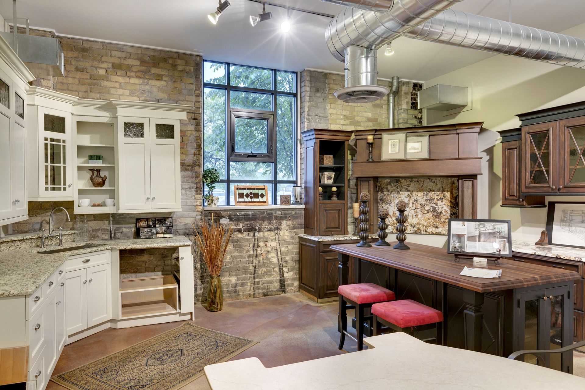 Showroom with white cabinetry, a stone-faced wall, a large black-framed window and a dark wood island with red stools