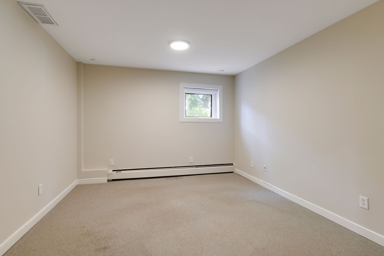 Unfurnished room with beige walls, beige carpet and a single window with a baseboard heater beneath