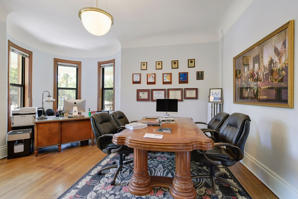 Office with an oval wooden table, black leather chairs, a bay window and framed certificates on the wall