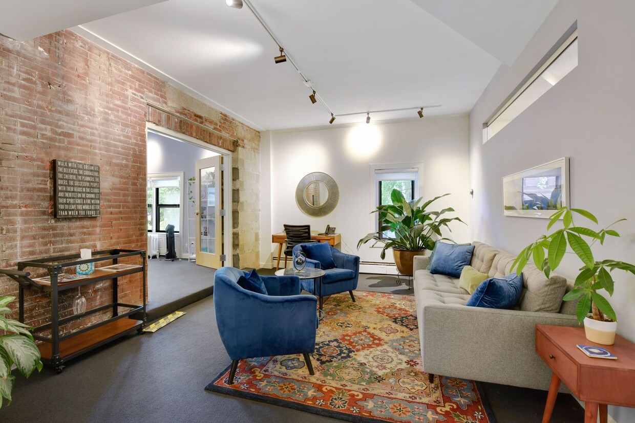 Shared lounge with an exposed brick wall, navy blue armchairs, a grey sofa, a patterned rug and track lighting