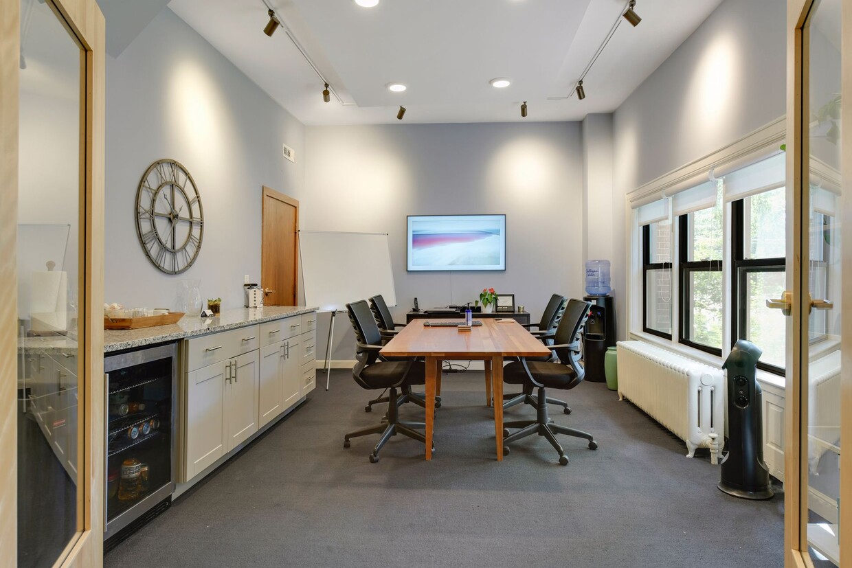 Conference room with a wooden table and black chairs, a wall-mounted display and a counter with a beverage refrigerator