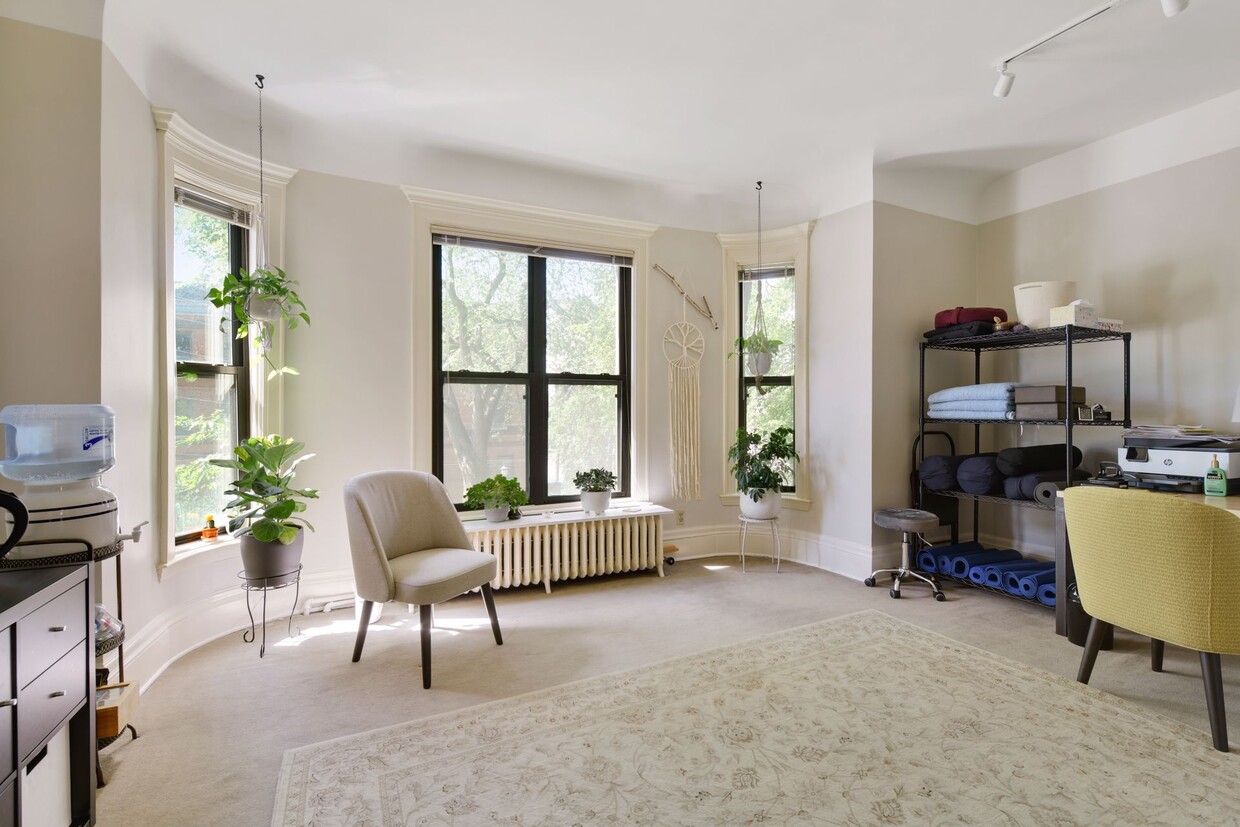 Bright suite with a curved bay of tall windows above a cast-iron radiator, an armchair and potted plants