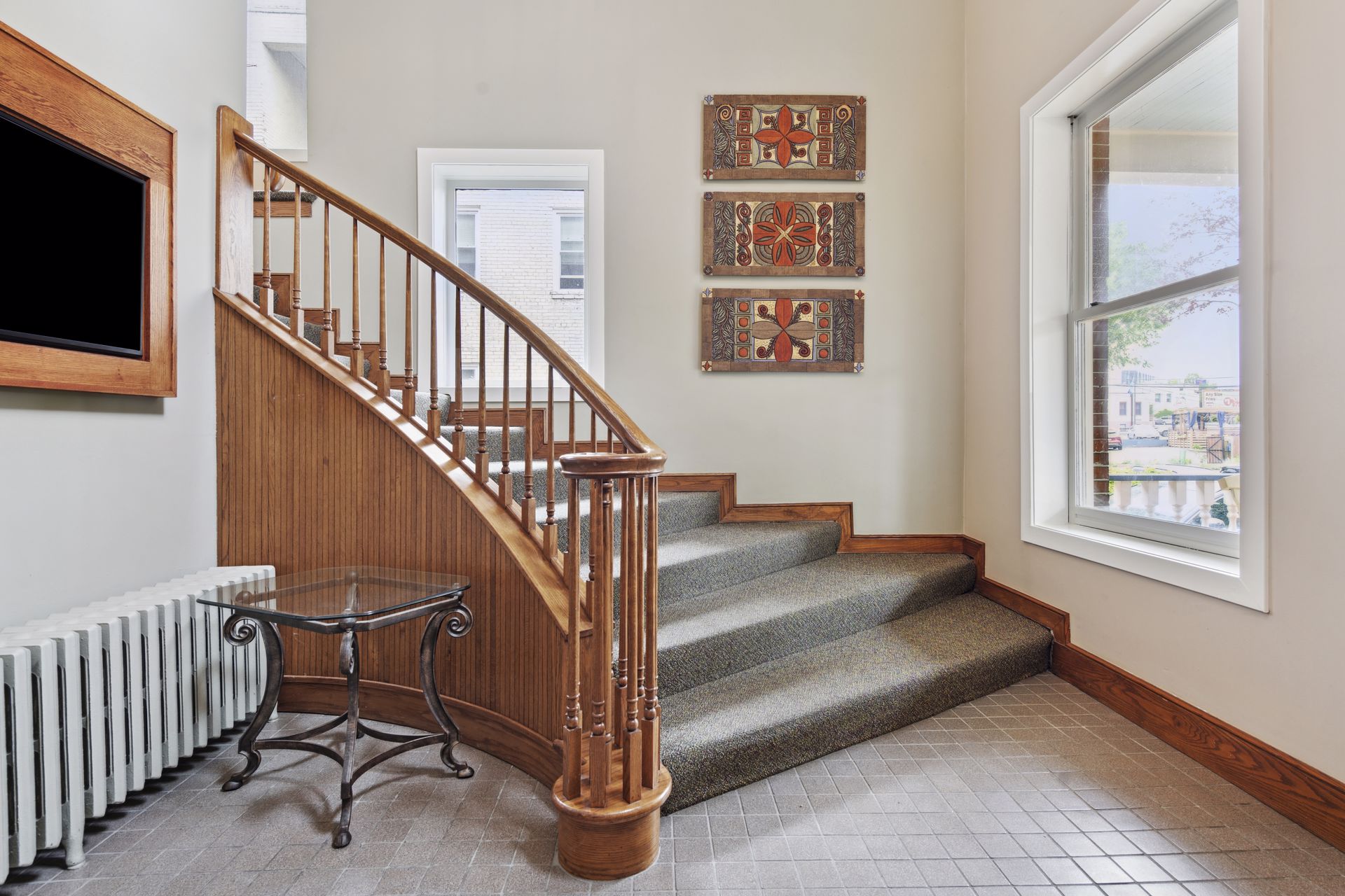 Interior stair hall with a curved oak staircase and turned newel post, a grey carpet runner and a cast-iron radiator