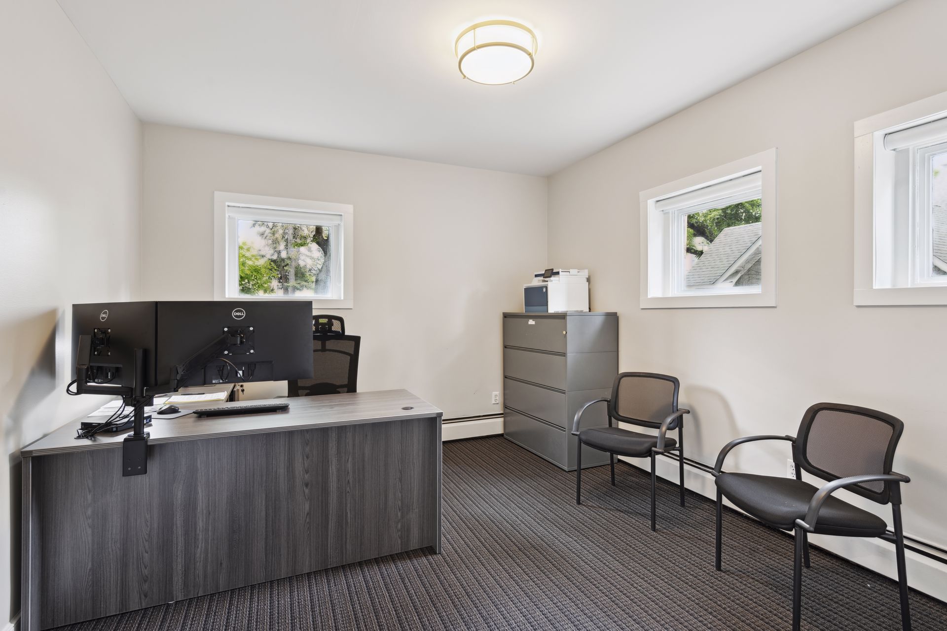Office with a grey desk, dual monitors, a lateral filing cabinet and two guest chairs