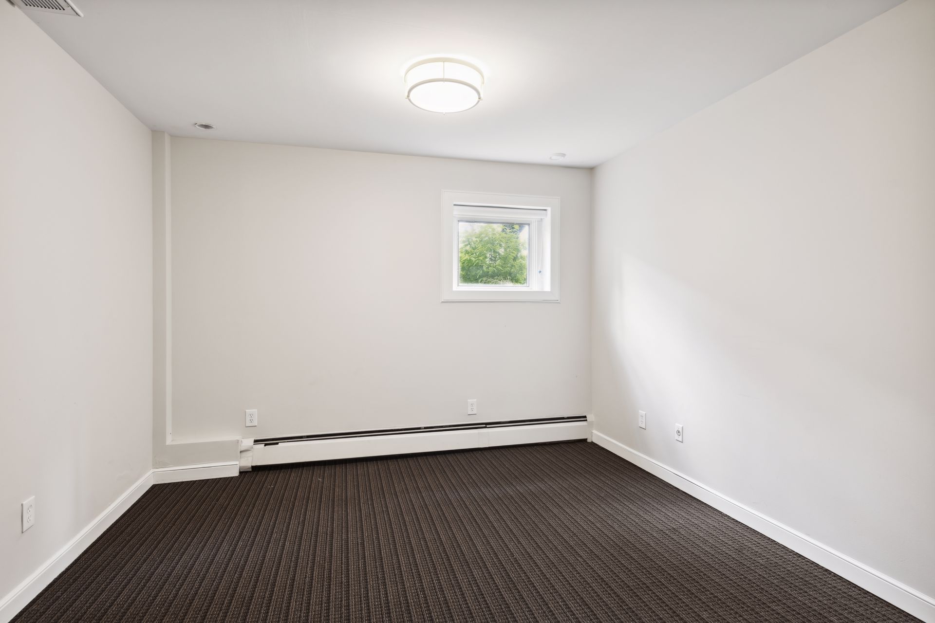 Unfurnished room with white walls, dark striped carpet and a window with a baseboard heater beneath