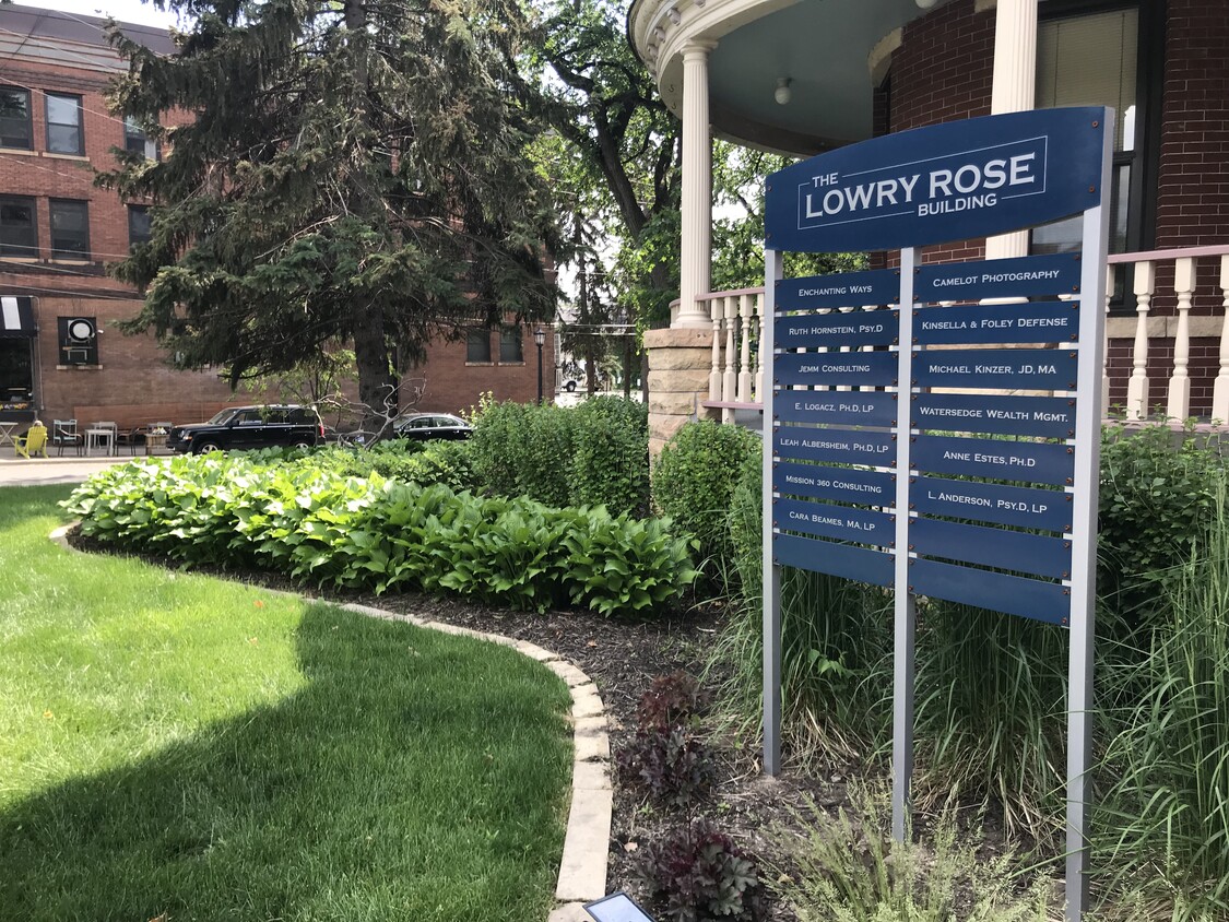 Freestanding blue directory sign reading The Lowry Rose Building beside a landscaped bed