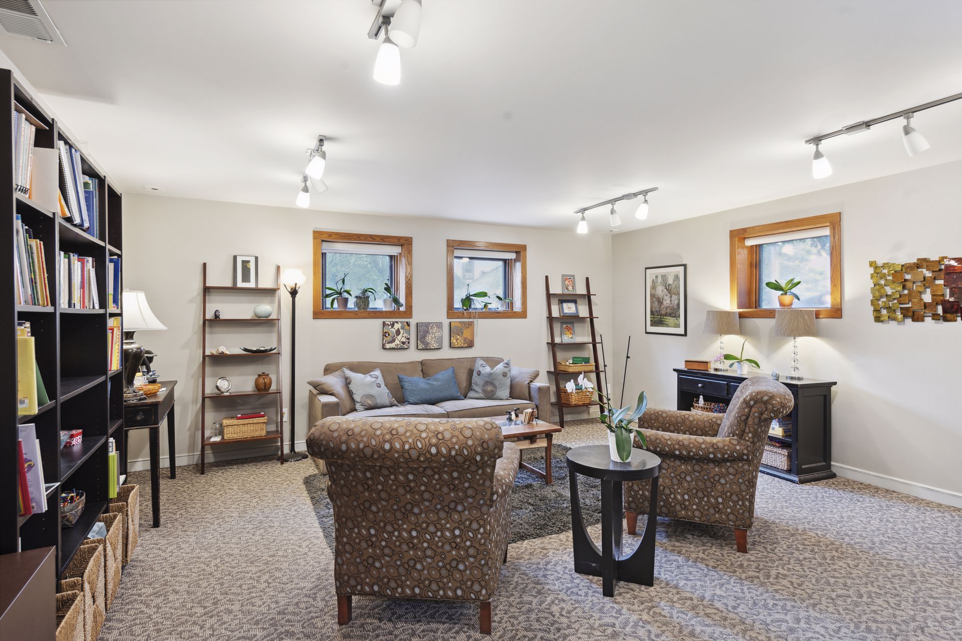 Garden-level lounge with tall black bookcases, patterned armchairs and a sofa
