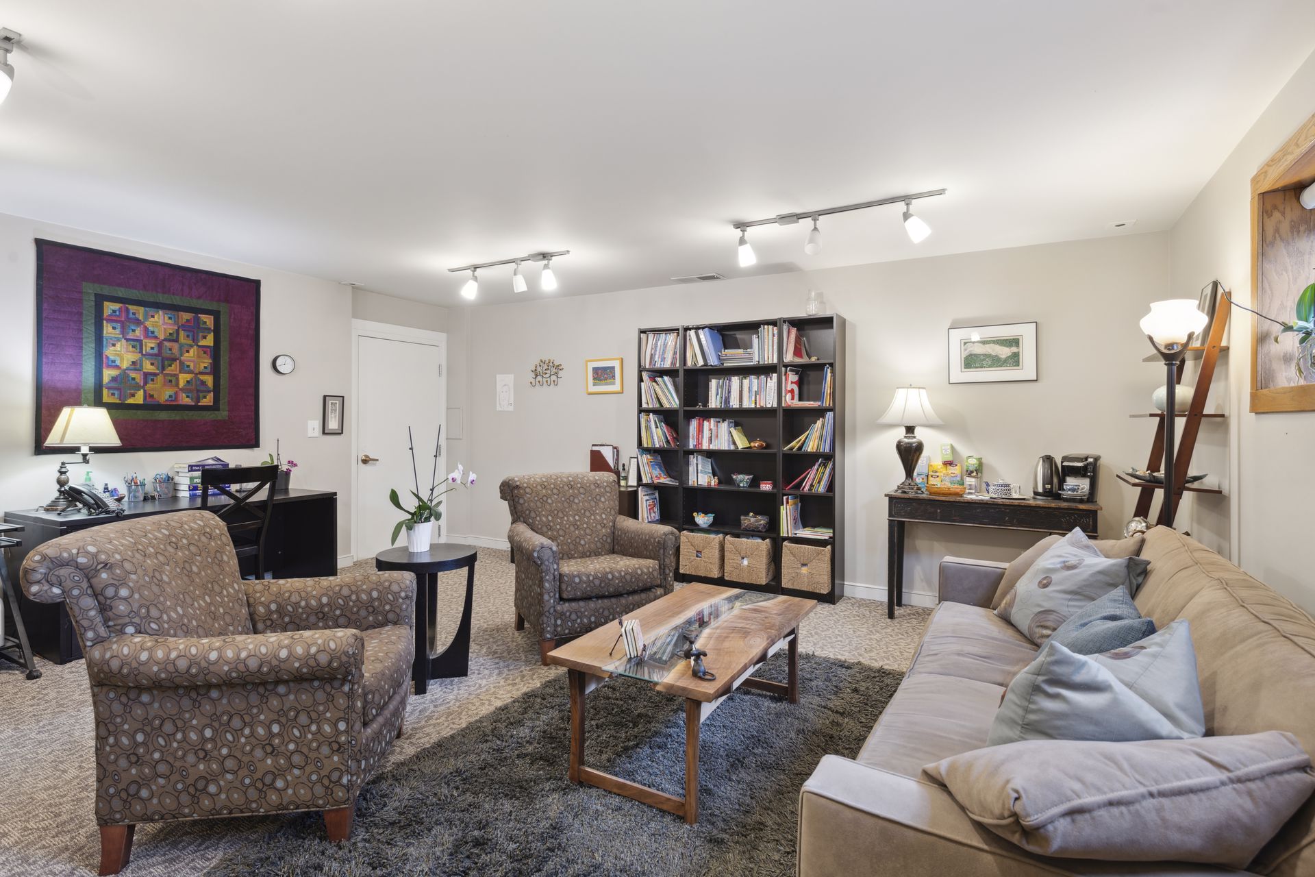 Garden-level lounge from a third angle with a quilt wall hanging and a desk
