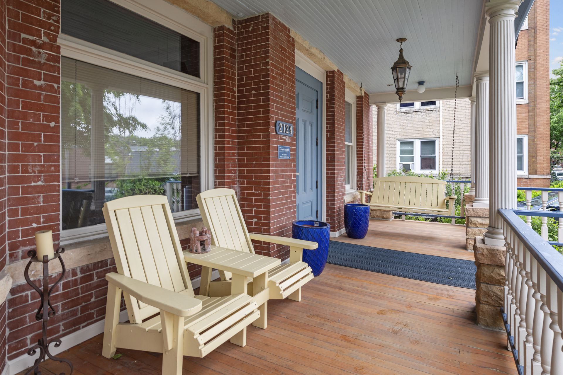 View along the porch deck past brick piers to a hanging lantern, a porch swing and blue glazed planters