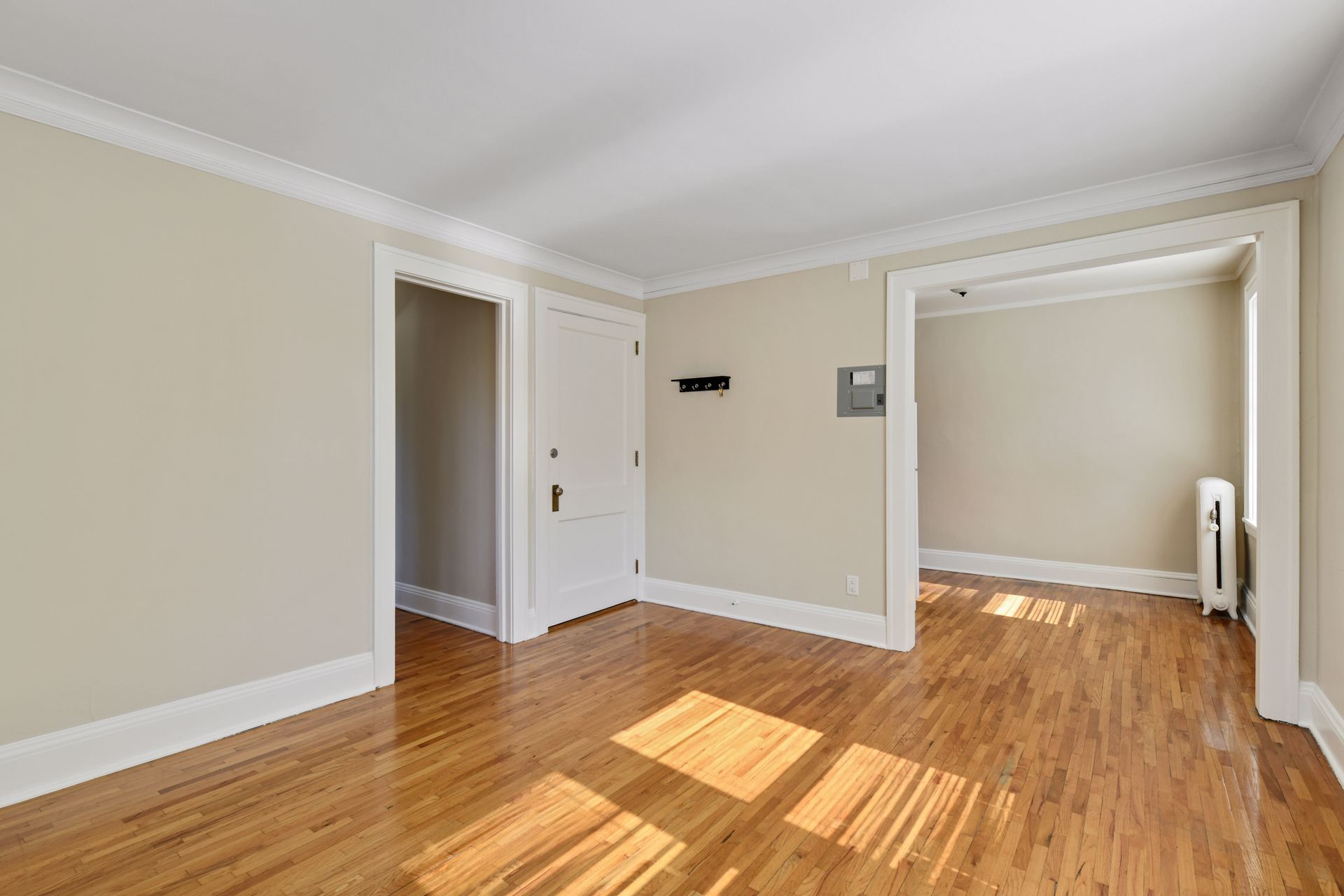 Empty room with a white panel door, a wall-mounted electrical panel and a cased opening to a second room