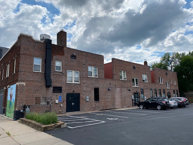 Wider view of the building's rear elevation and chimney from the parking lot, with a painted mural panel at the left end