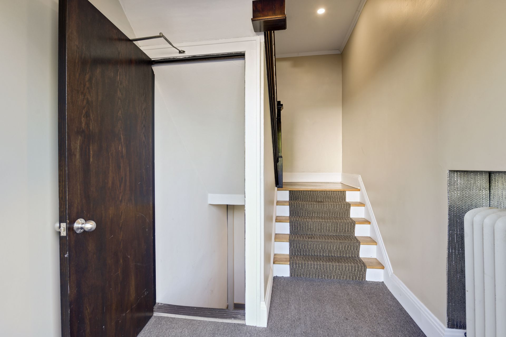Carpeted stair landing with a dark stained wood door and a cast-iron radiator