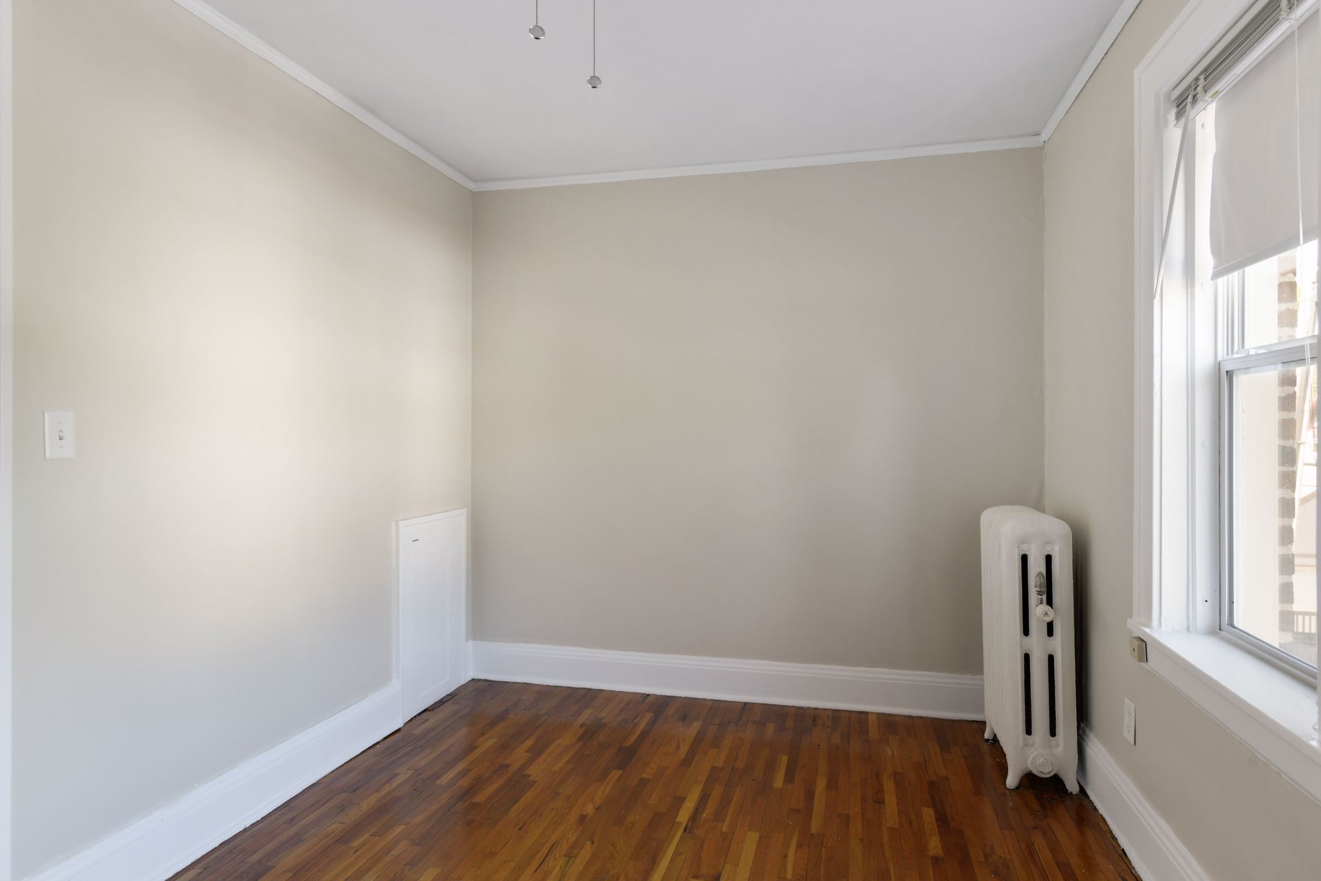 Small empty room with one window and a cast-iron radiator beneath it