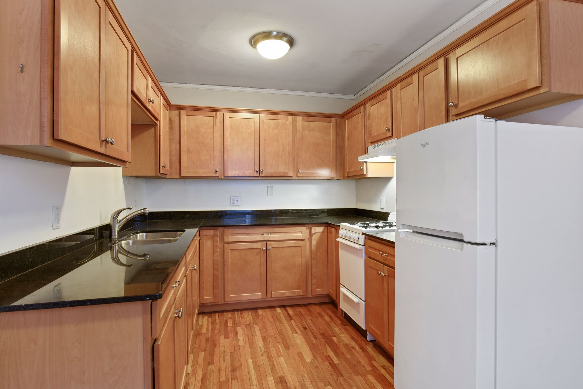 Apartment kitchen with wood cabinets, dark stone countertops, a white gas range and a refrigerator