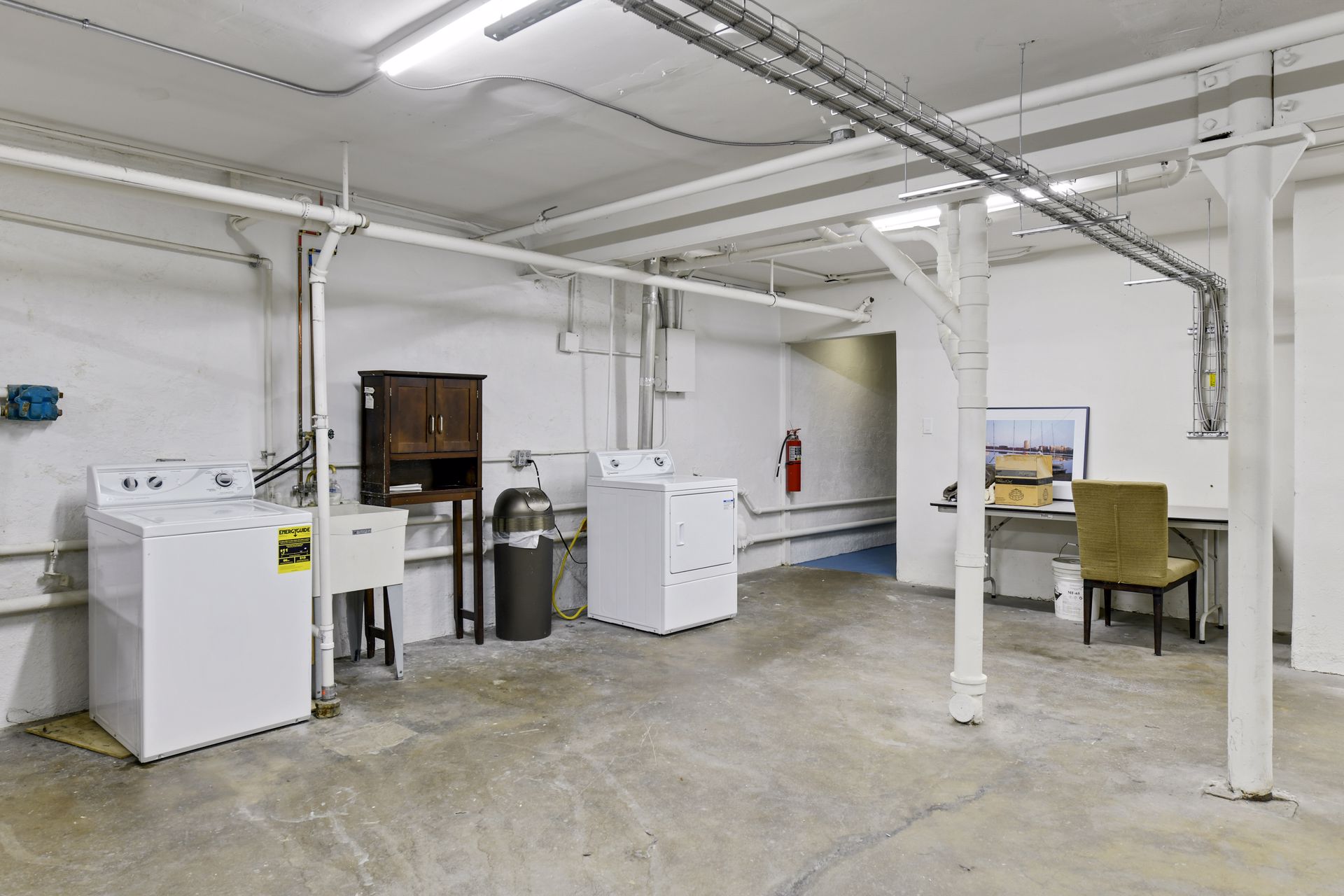 Basement laundry room with two washing machines, a dryer, a utility sink and a desk