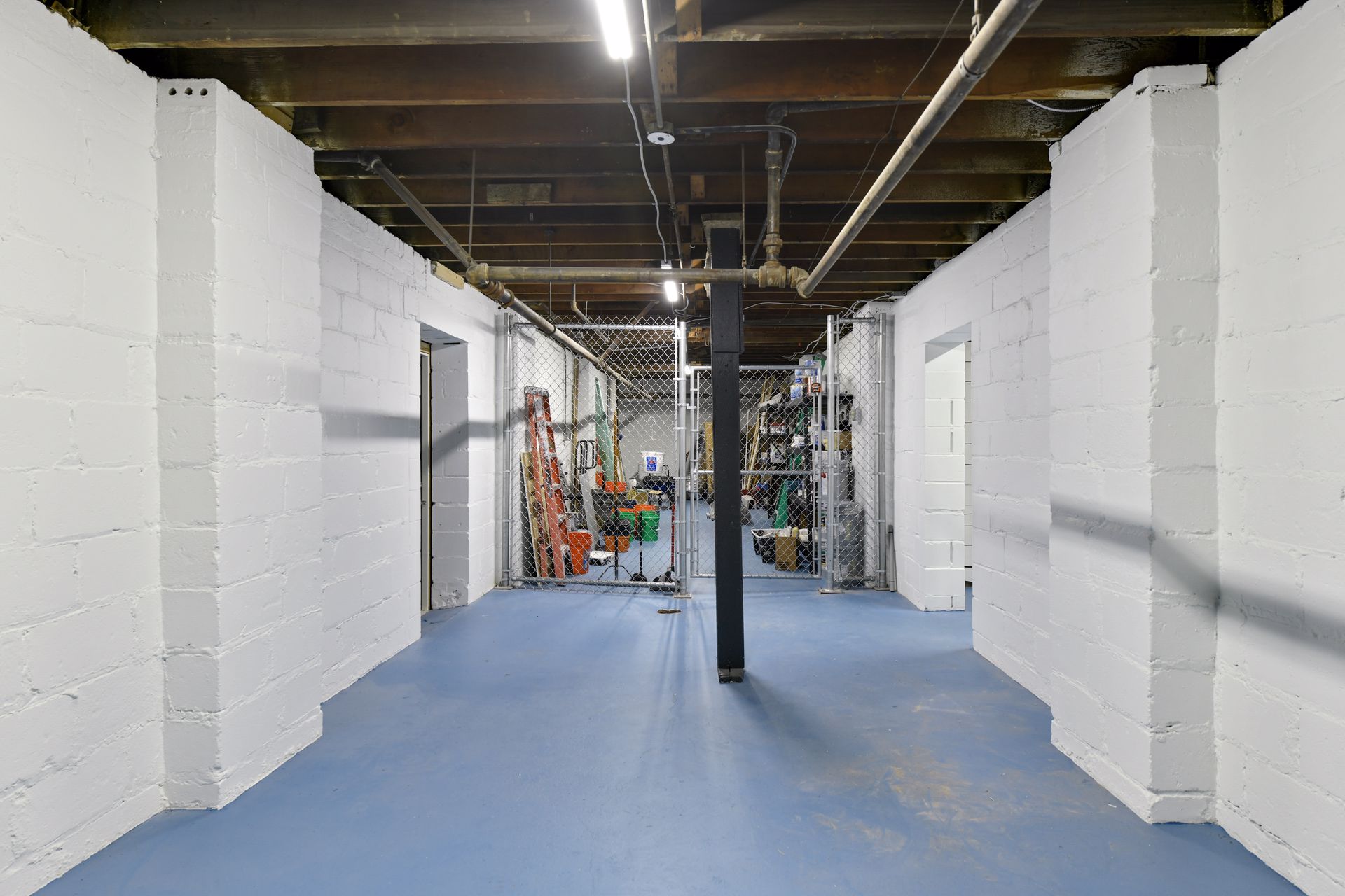 Basement corridor between whitewashed block storage rooms with a blue painted floor