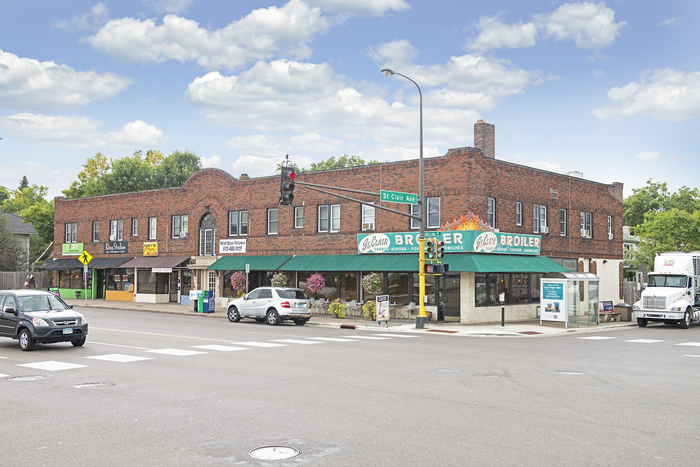 Corner view of the St. Clair Building, a two-storey red brick building with ground-floor storefronts under a green awning and apartment windows above