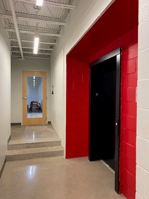 Corridor with concrete block walls, a corrugated metal deck ceiling and a red-painted door surround