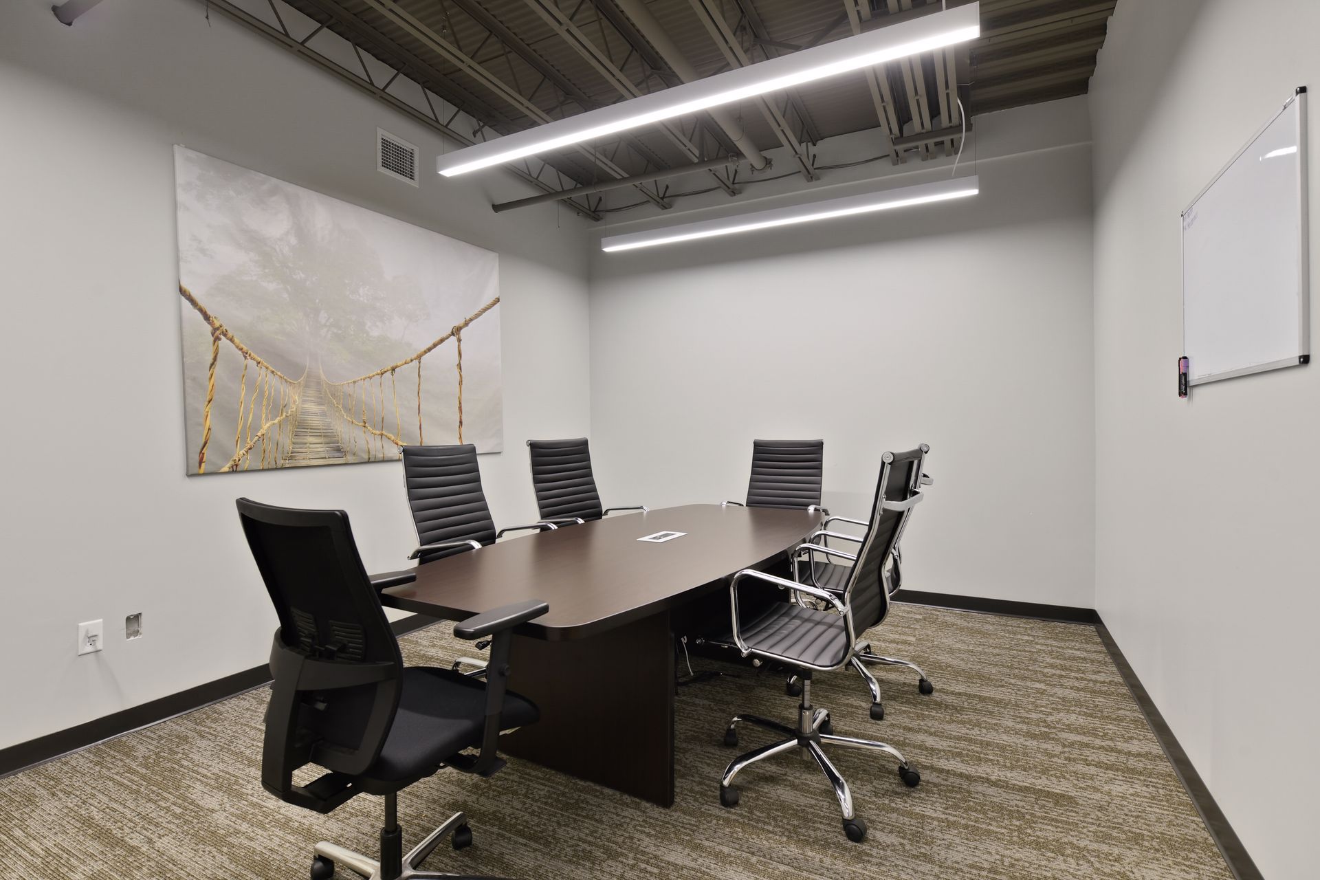 Conference room with a boat shaped table, black leather chairs, canvas artwork and a whiteboard