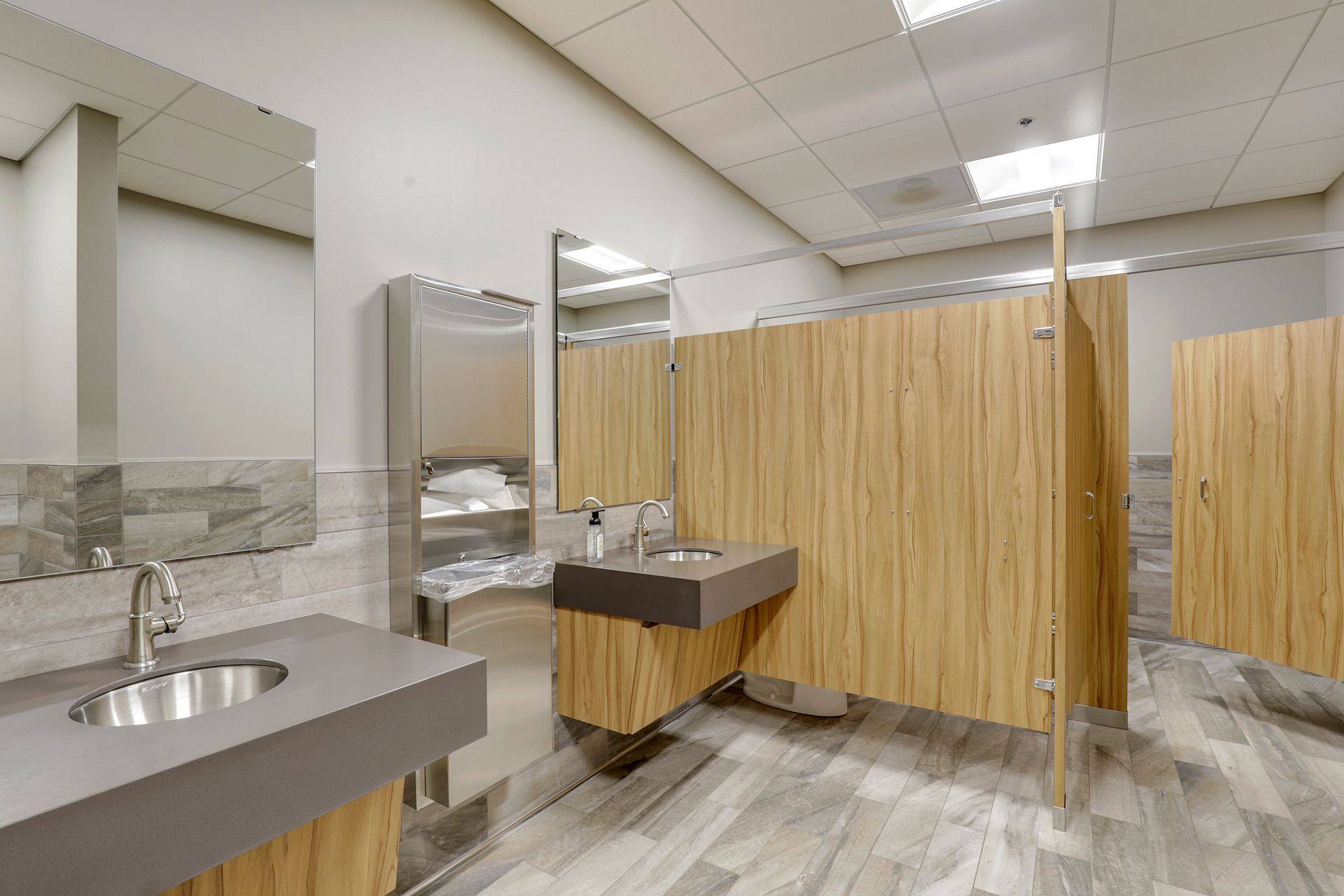 Restroom with two wall hung sinks, wood grain partitions and stone look tile