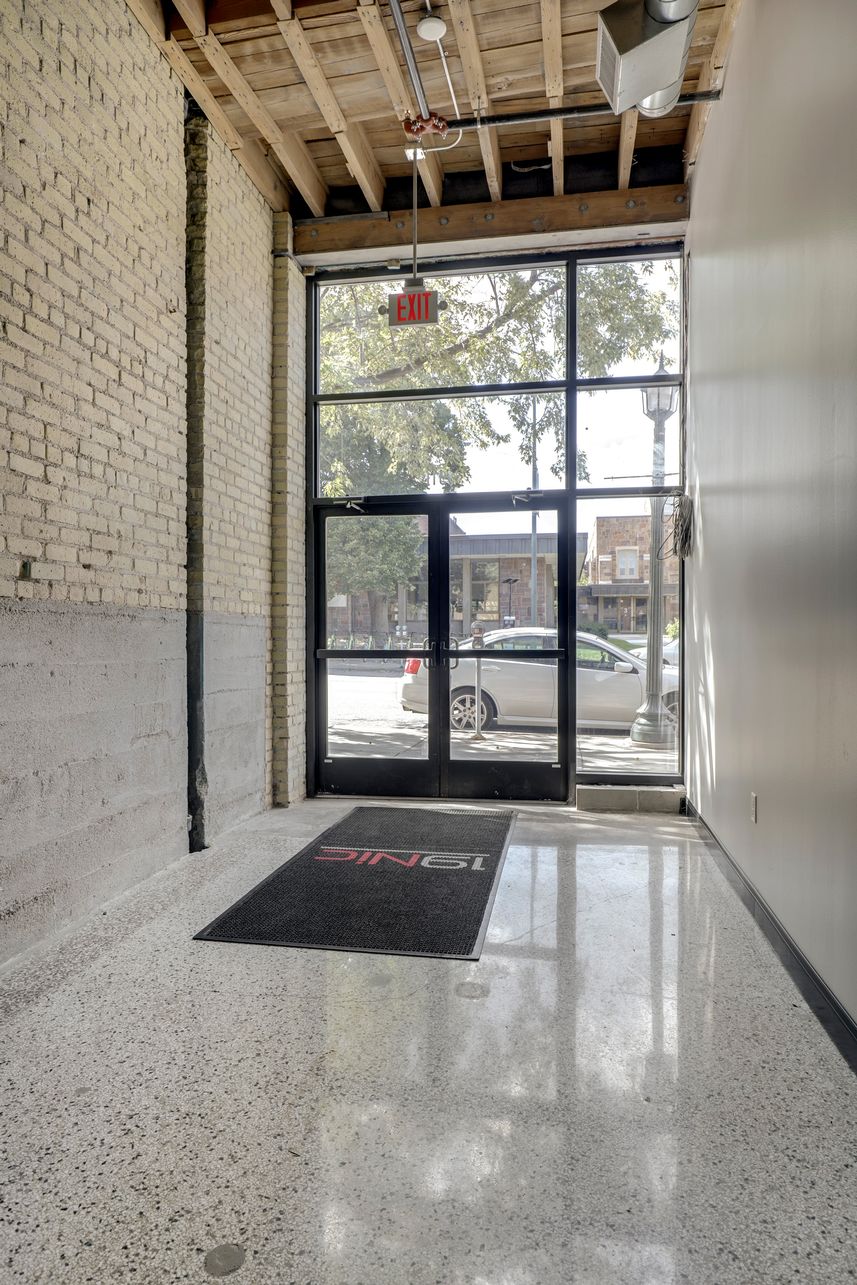Entrance vestibule with a 19NIC logo floor mat, painted brick wall and full height glazed doors onto the street
