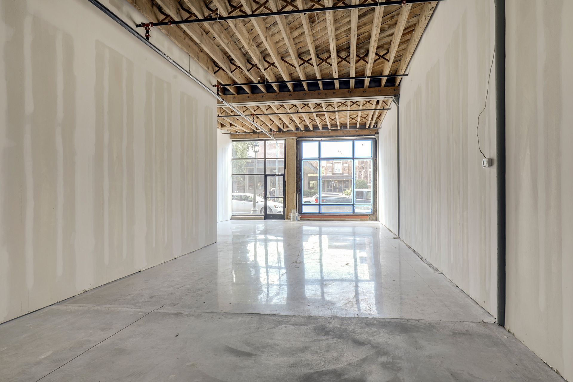 Narrow unfinished suite with white walls, exposed wood ceiling joists and a storefront window at the far end