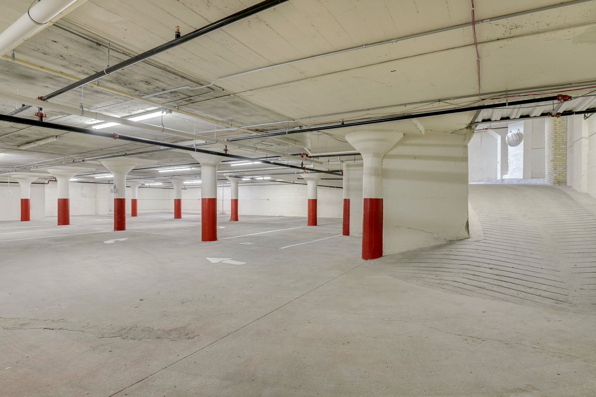 Enclosed parking deck with concrete columns, painted white with red column bases and striped stalls