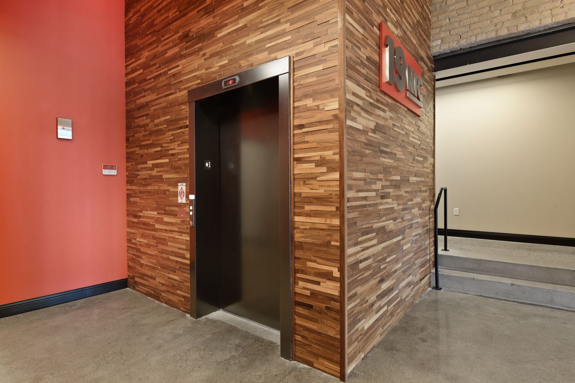 Elevator doors set into a wood slat surround beside an orange red painted wall