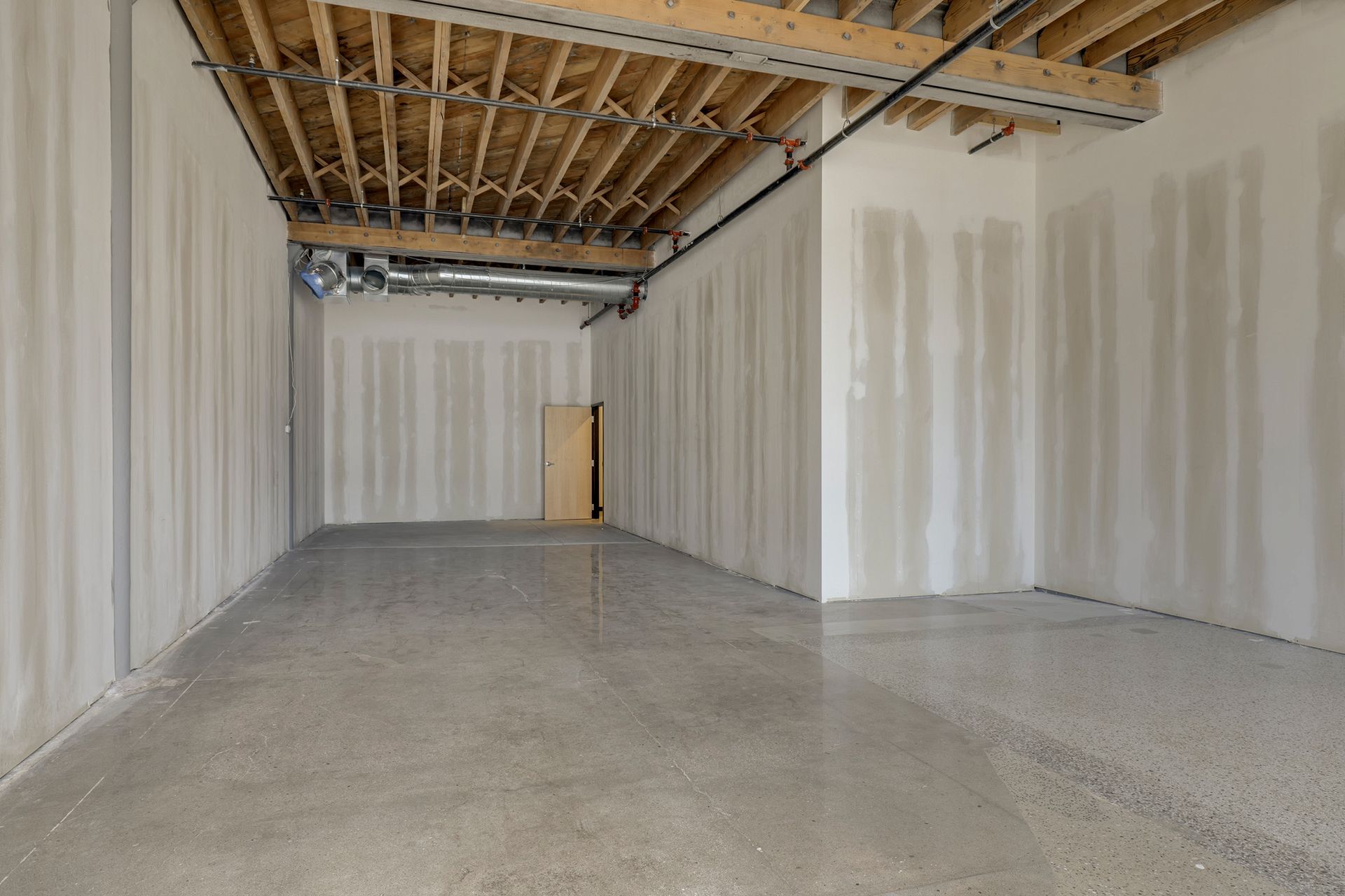 Narrow white walled space with exposed wood joists and a spiral duct running the length of the ceiling