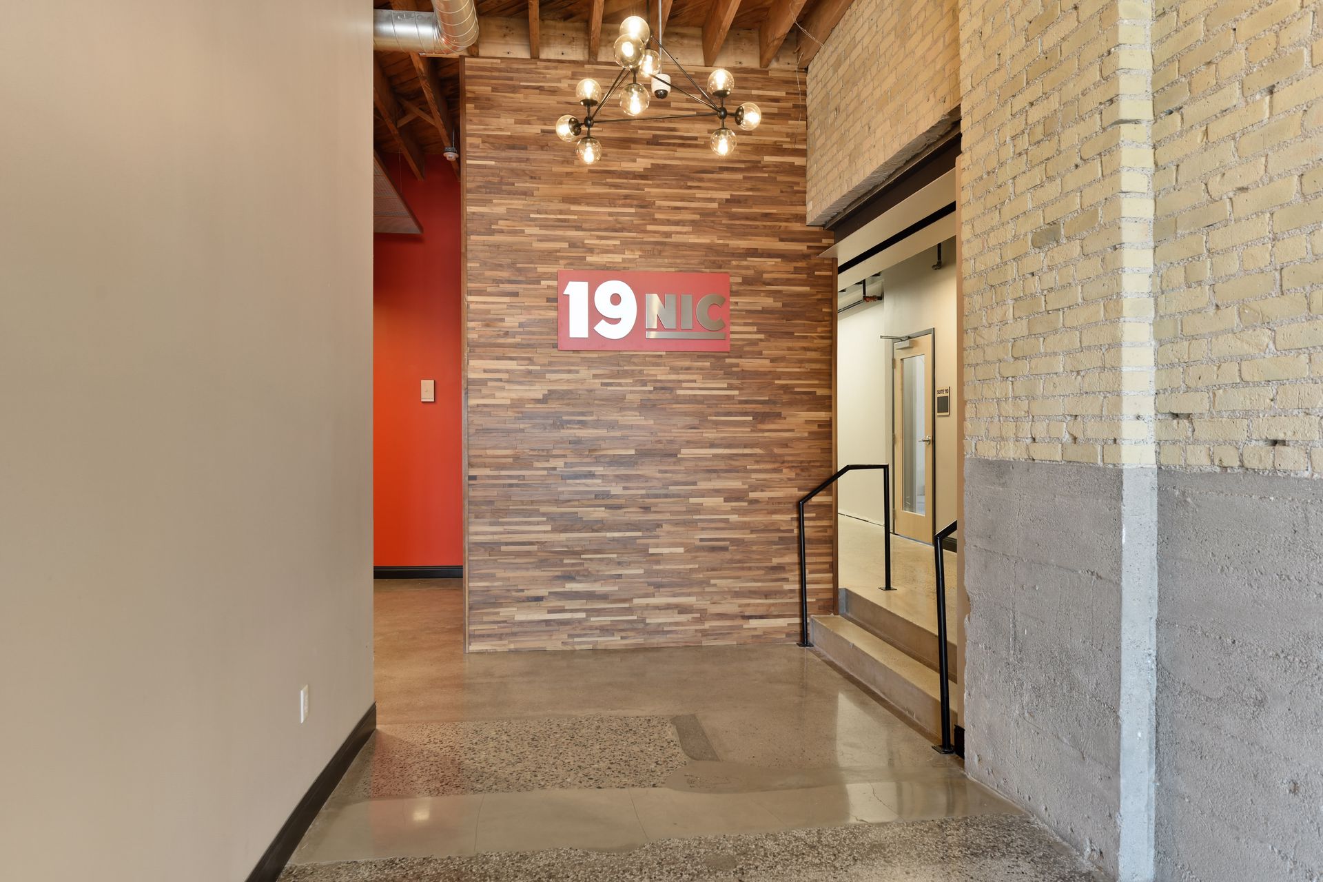 Lobby with a red 19 NIC sign on a stacked stone wall, a globe cluster pendant light and polished terrazzo flooring