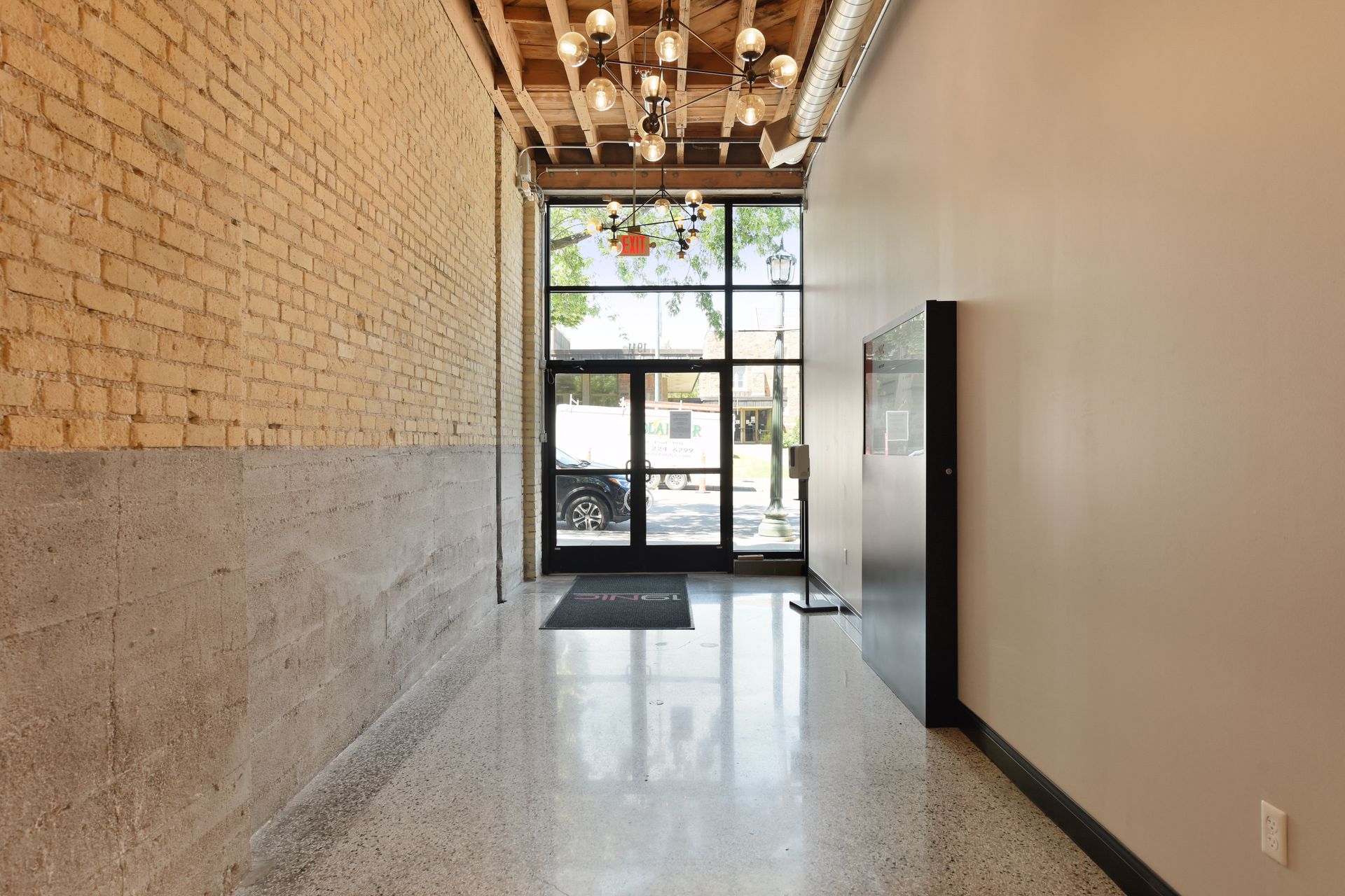 Ground floor corridor with exposed brick and wood ceiling joists leading to glazed entry doors