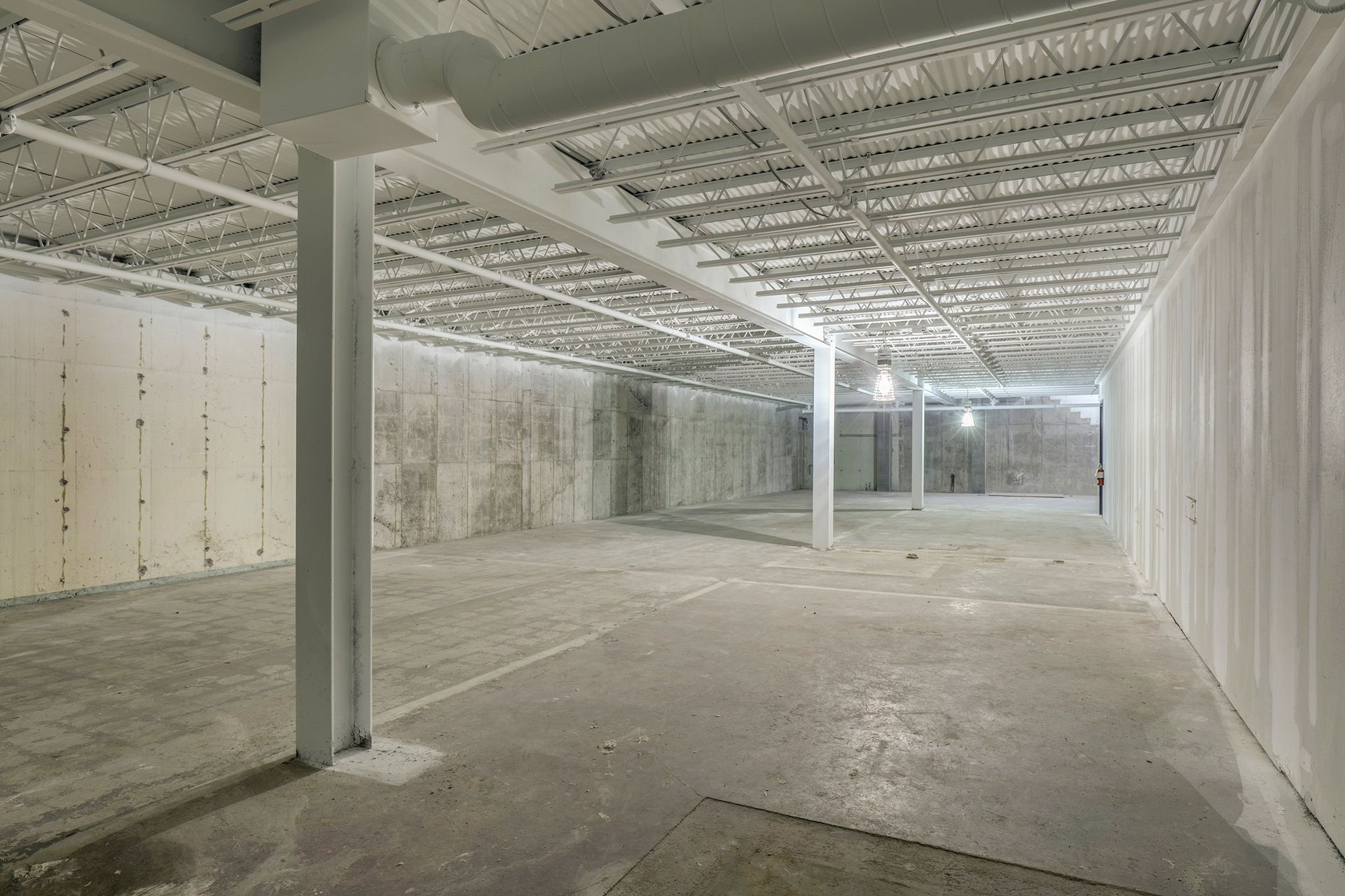 Lower level with steel bar joists, a painted white beam and concrete walls