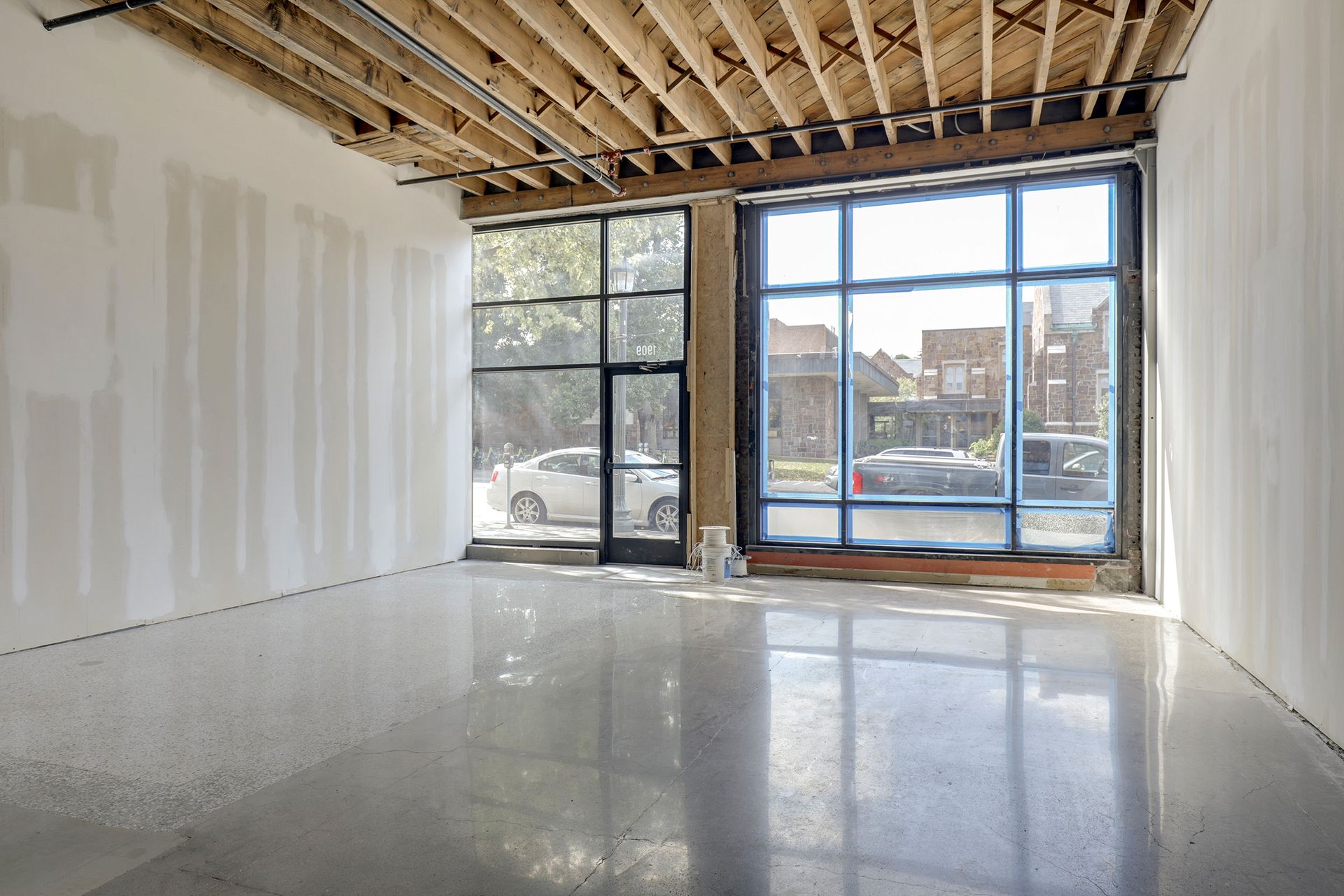 Empty retail bay with two storefront windows onto the street, white walls, exposed joists and a polished floor