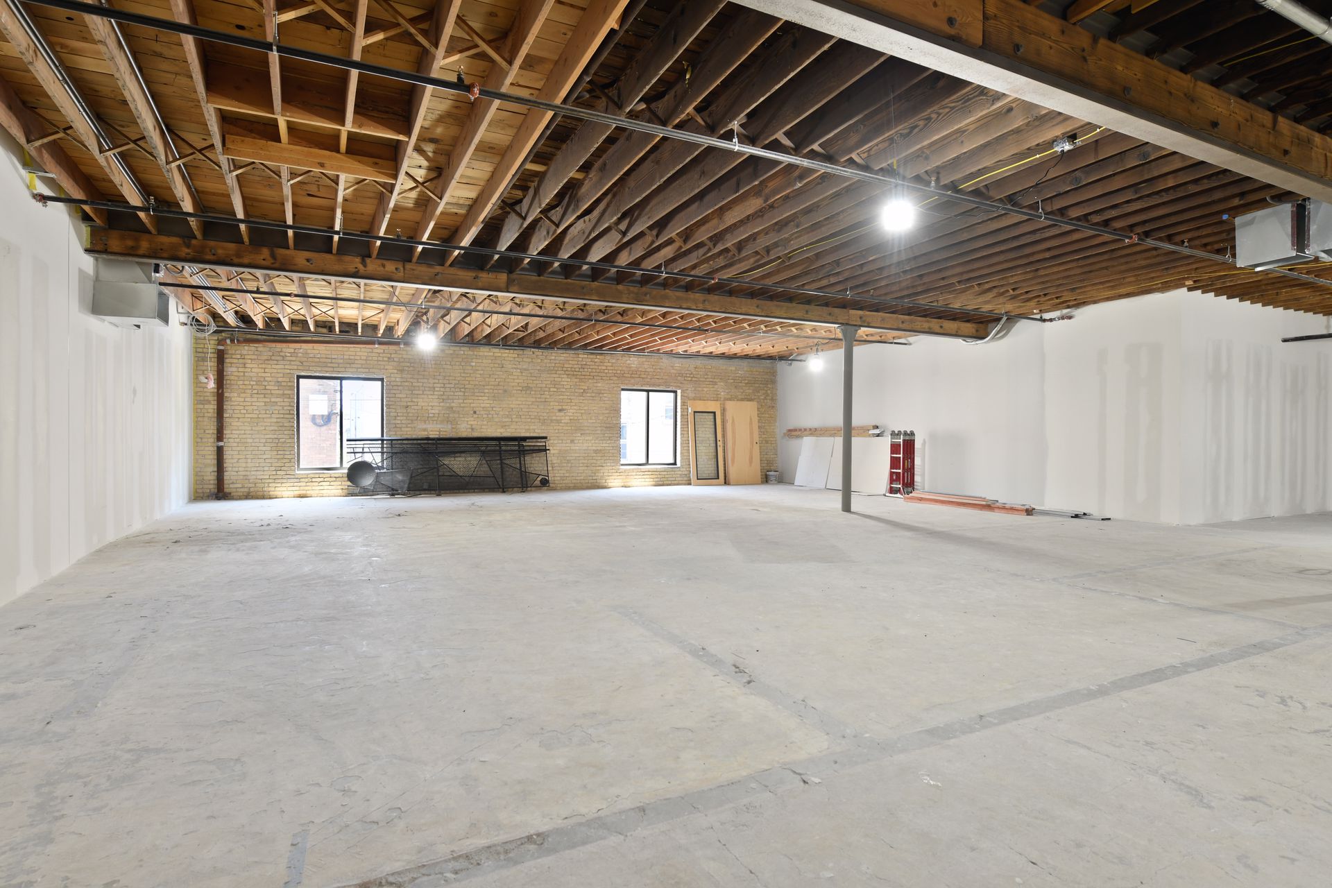Empty floor with exposed joists, a cream brick end wall and two small windows