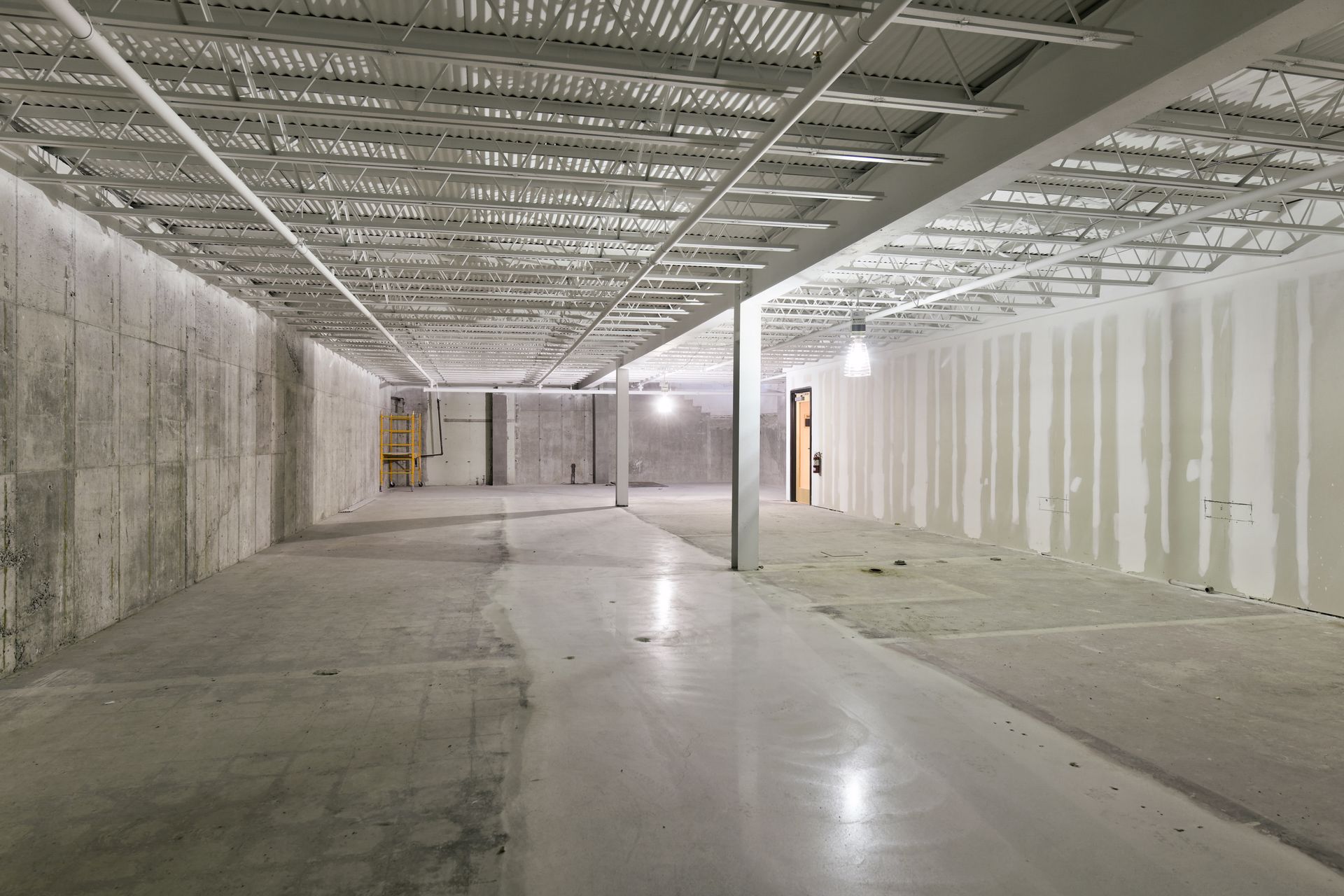 Lower level during construction with steel bar joists, concrete walls and taped drywall
