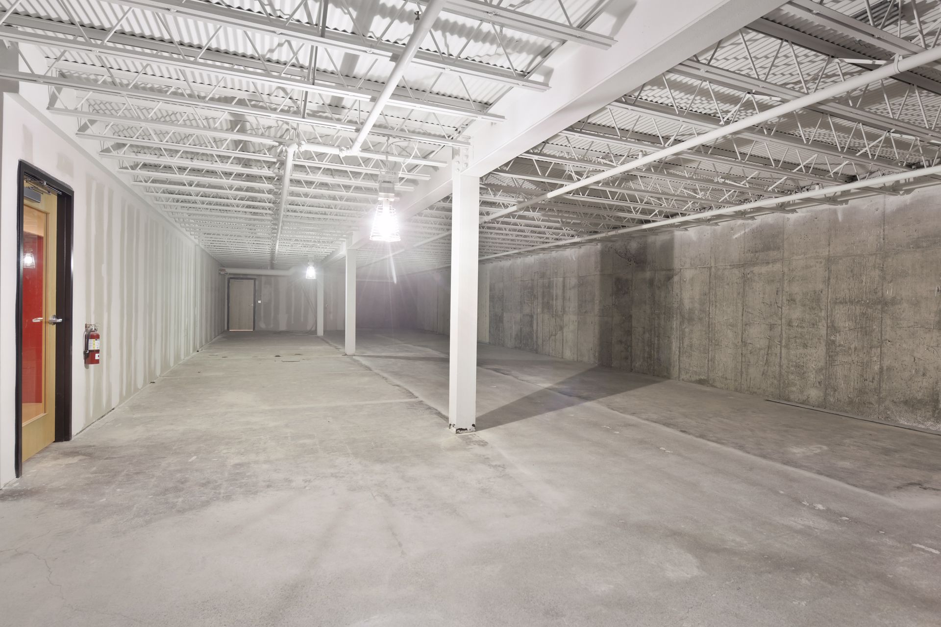 Lower level during construction with exposed steel bar joists, concrete walls and a red door