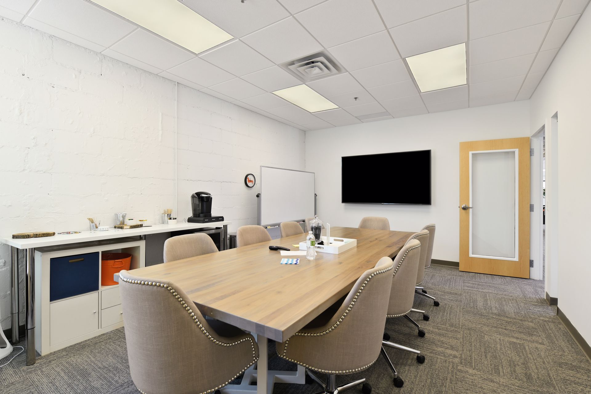Conference room with a wood table, upholstered chairs, a wall mounted display and painted brick