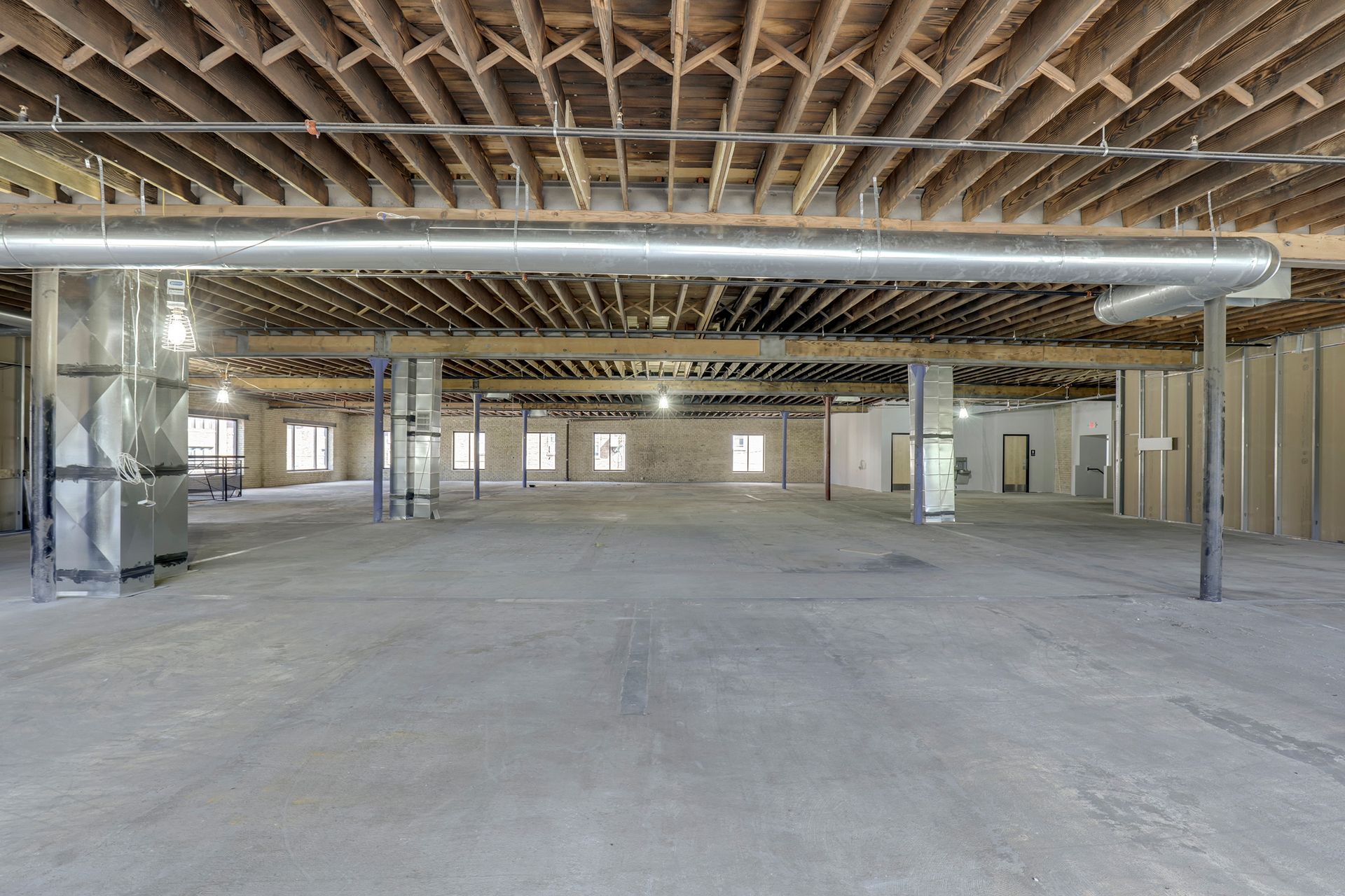 Empty floor plate with exposed joists, spiral ductwork and a furnace unit at left