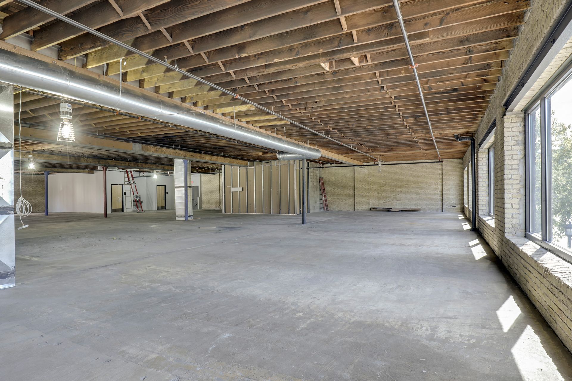 Empty floor plate with exposed joists, cream brick and a window wall at right