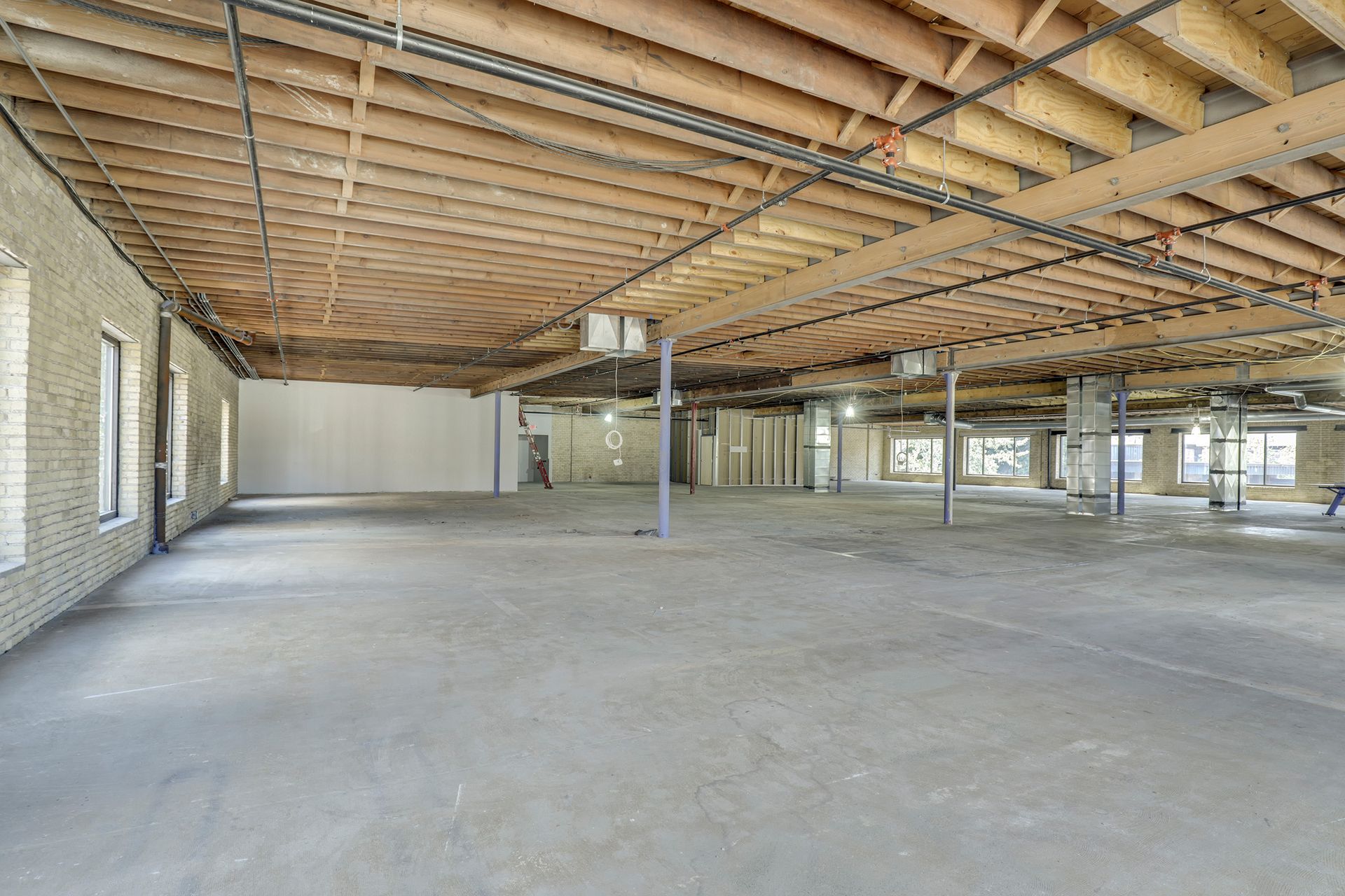 Empty floor plate with exposed wood joists and cream brick at the left-hand wall