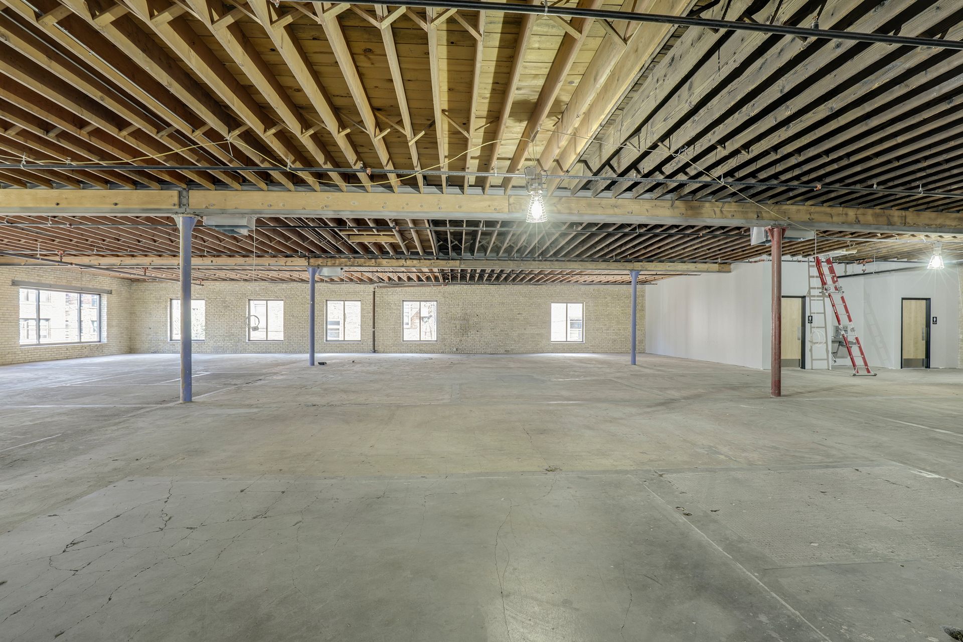 Empty floor plate with exposed joists, brick walls, punched windows and a red ladder