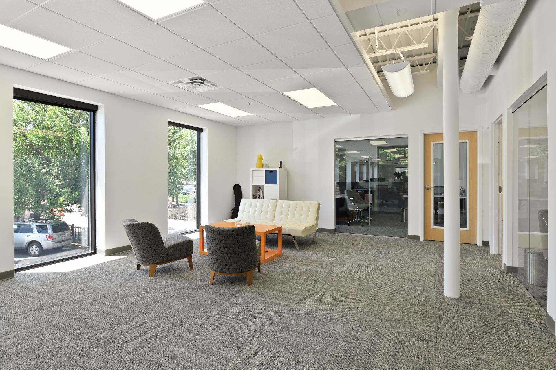 Suite reception and waiting area with a settee, two lounge chairs and glass fronted offices beyond