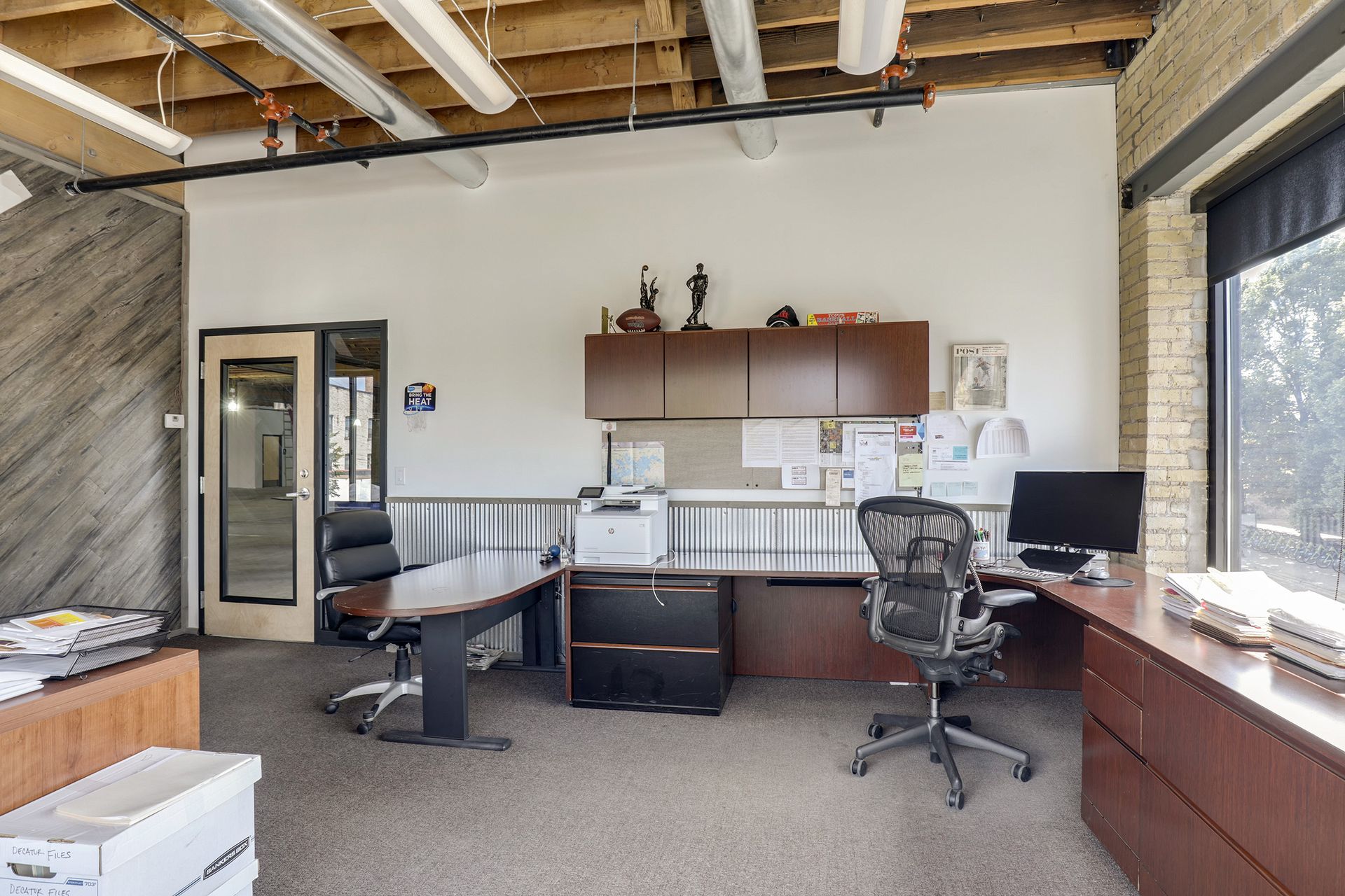 Occupied office with corrugated metal wainscot, overhead cabinets and a printer