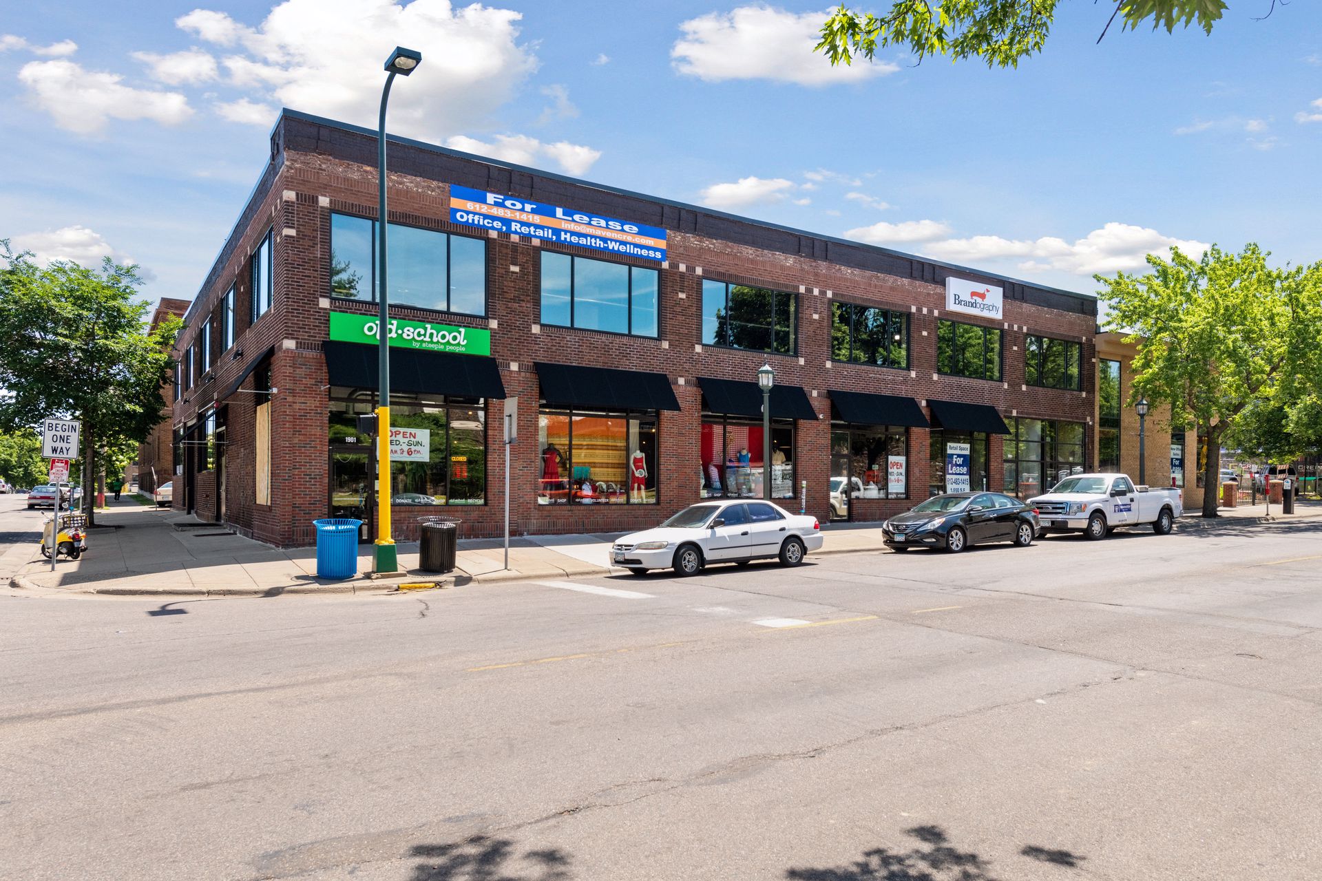 Corner view of the two-storey brick building with awninged storefronts and a For Lease banner above