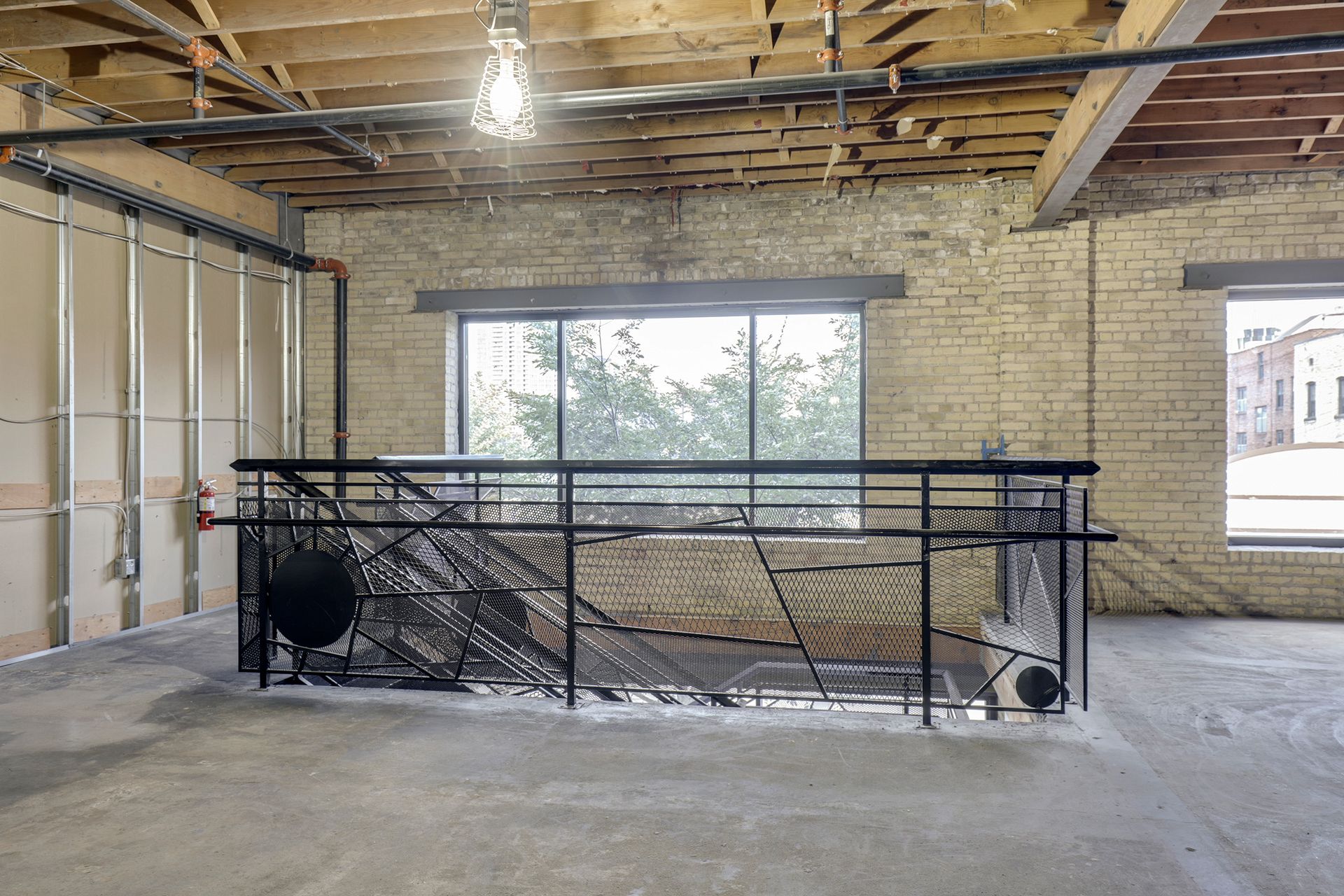 Upper floor space with exposed joists, a wide plate glass window and a black metal railing enclosing a floor opening