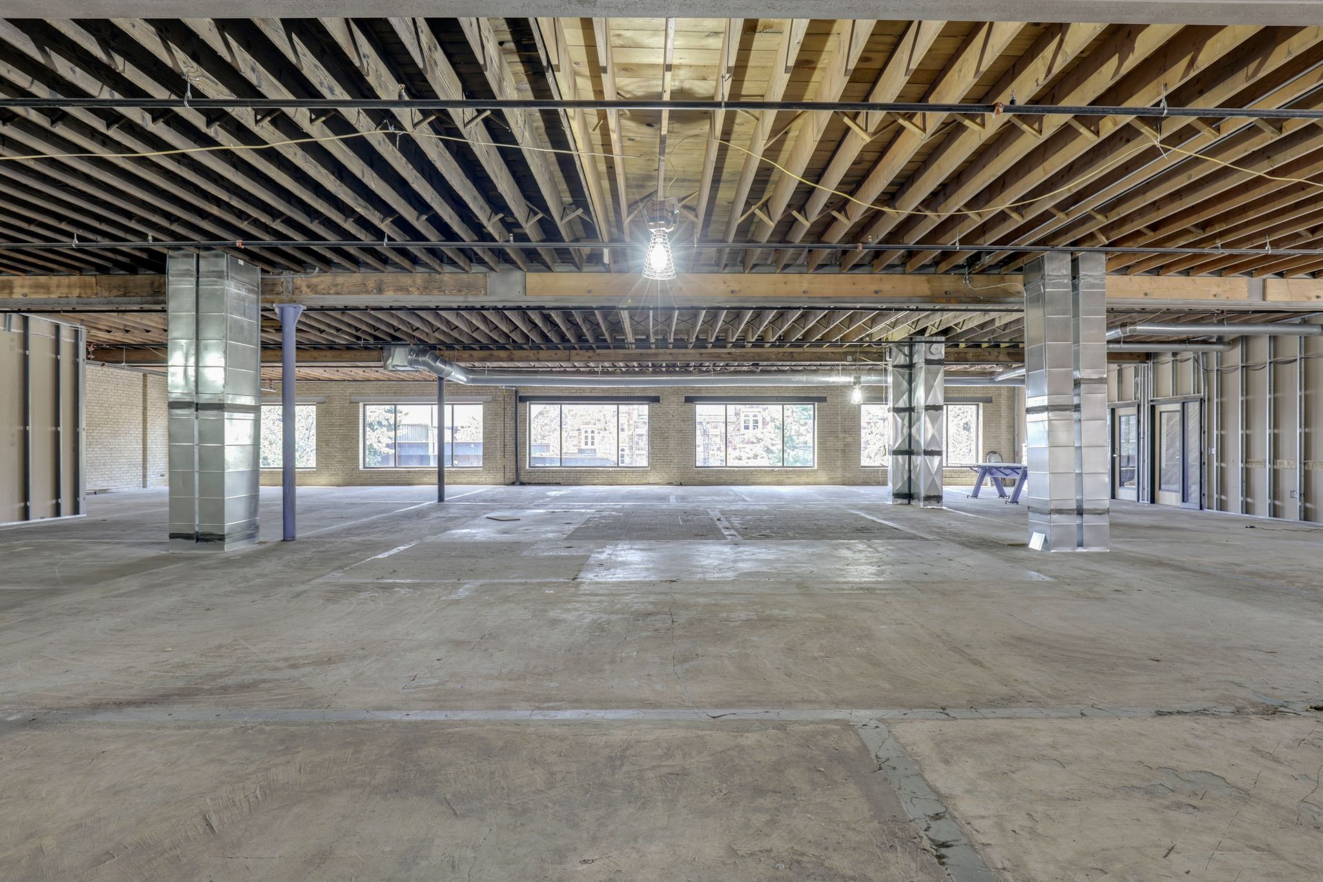 Empty floor plate with blackened joists, brick-clad piers and storefront glazing