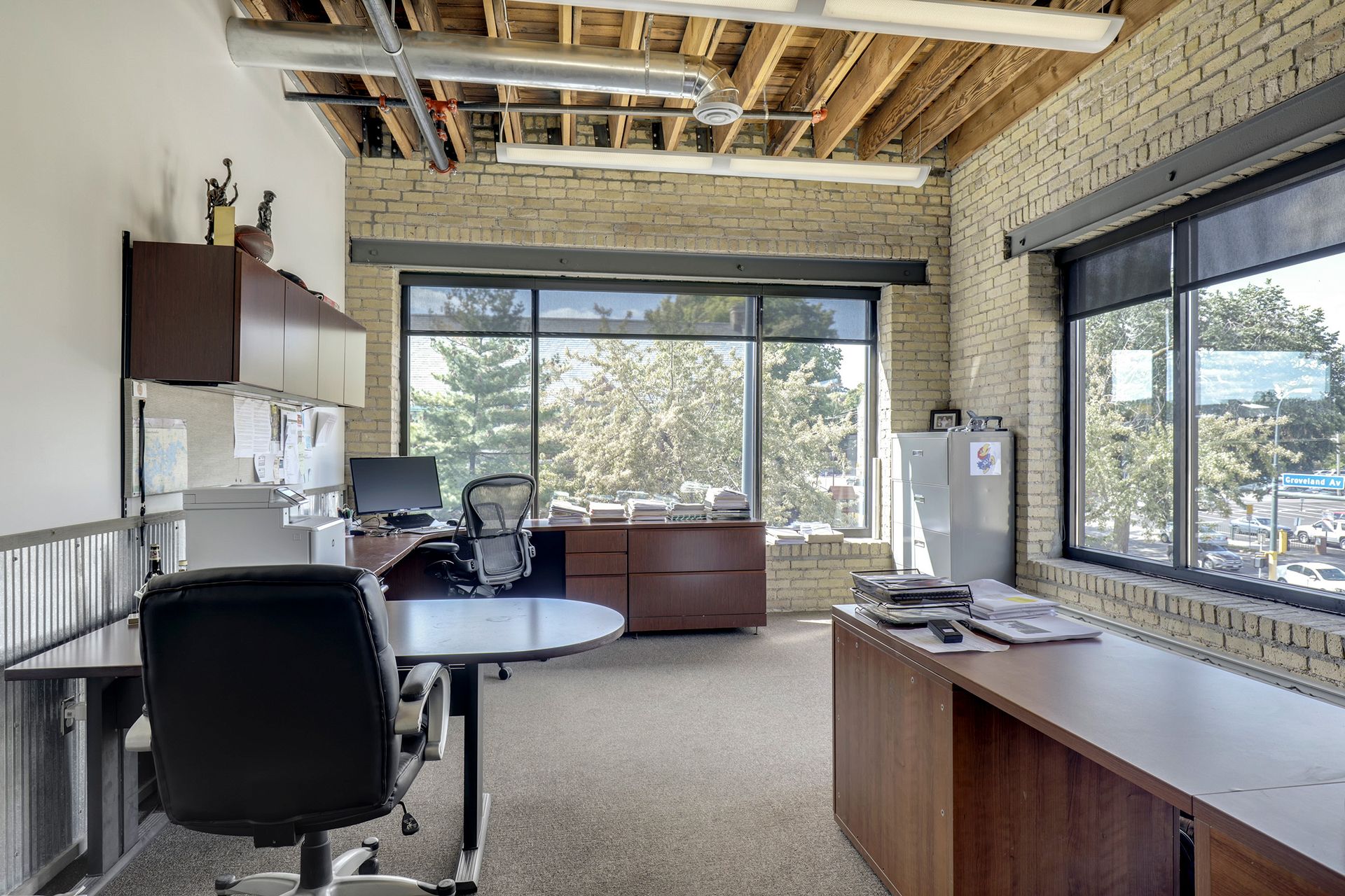 Occupied office with exposed wood joists, cream brick walls and a window looking onto trees