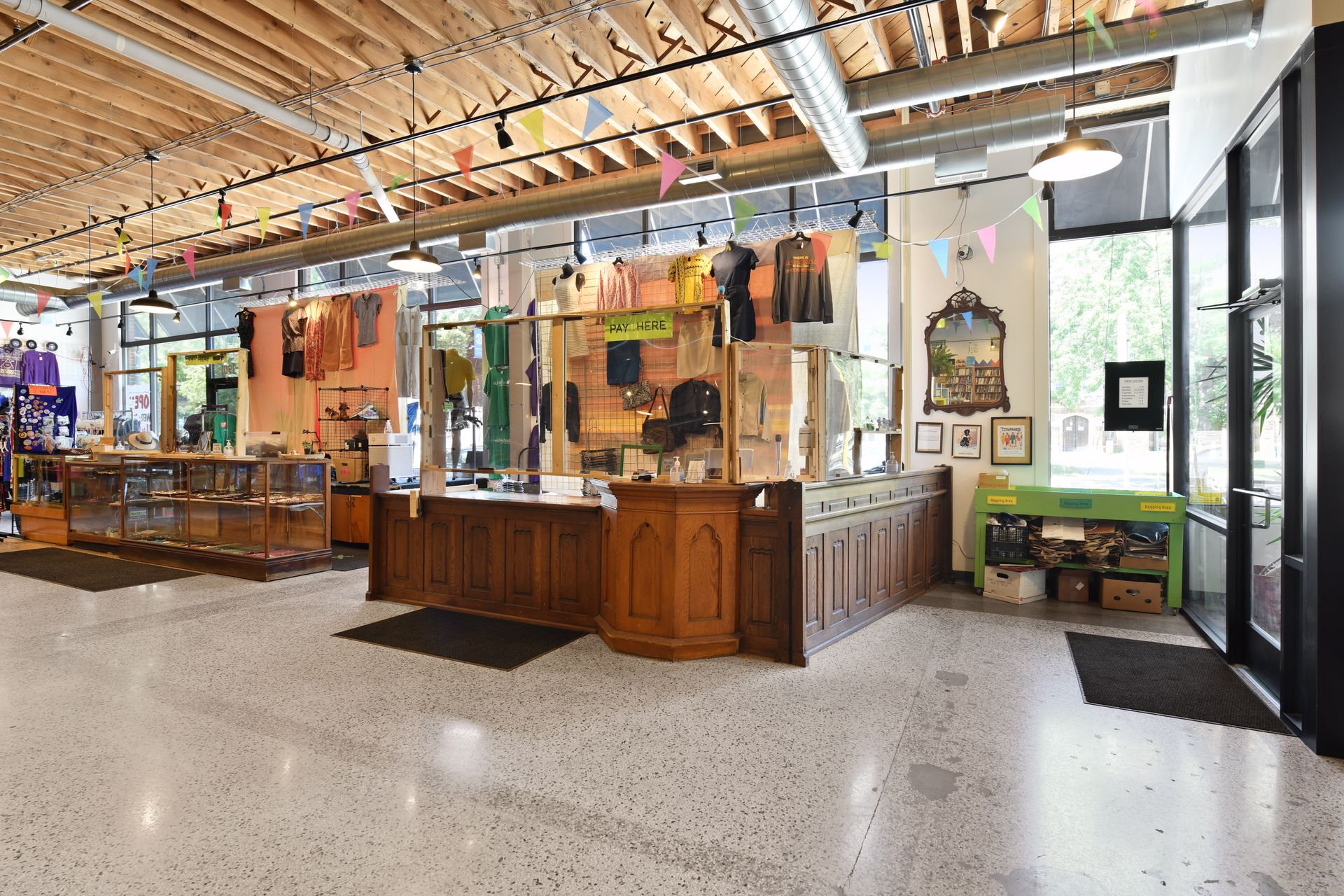 Retail space with a carved wood service counter, glass display cases and bunting beneath an exposed wood ceiling