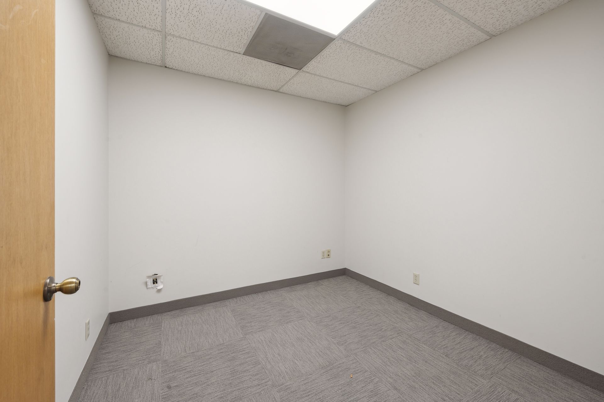 Small empty office room with a wood door and carpet tile flooring