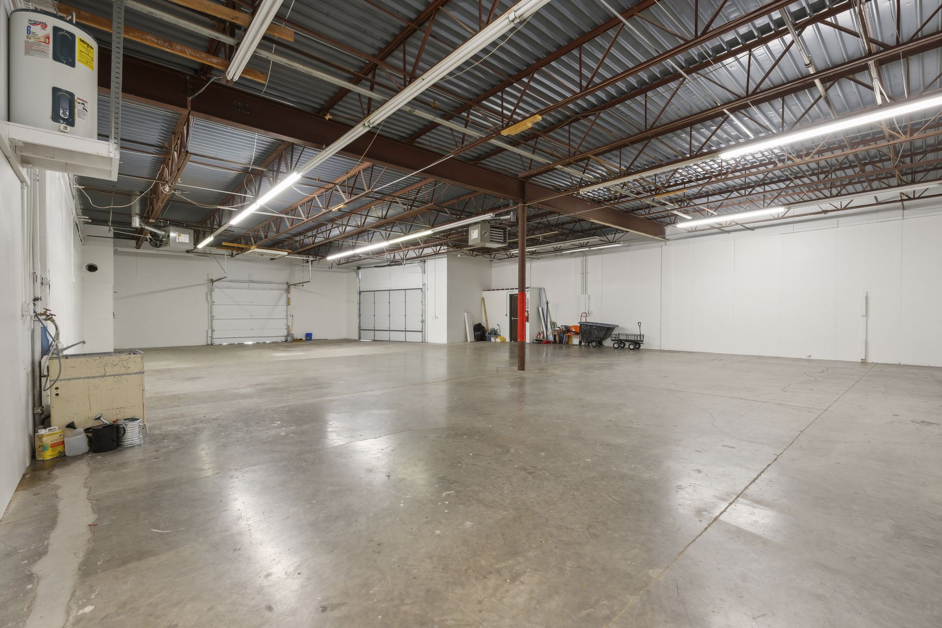 Warehouse bay with a sealed concrete floor, exposed steel joists and two white overhead doors